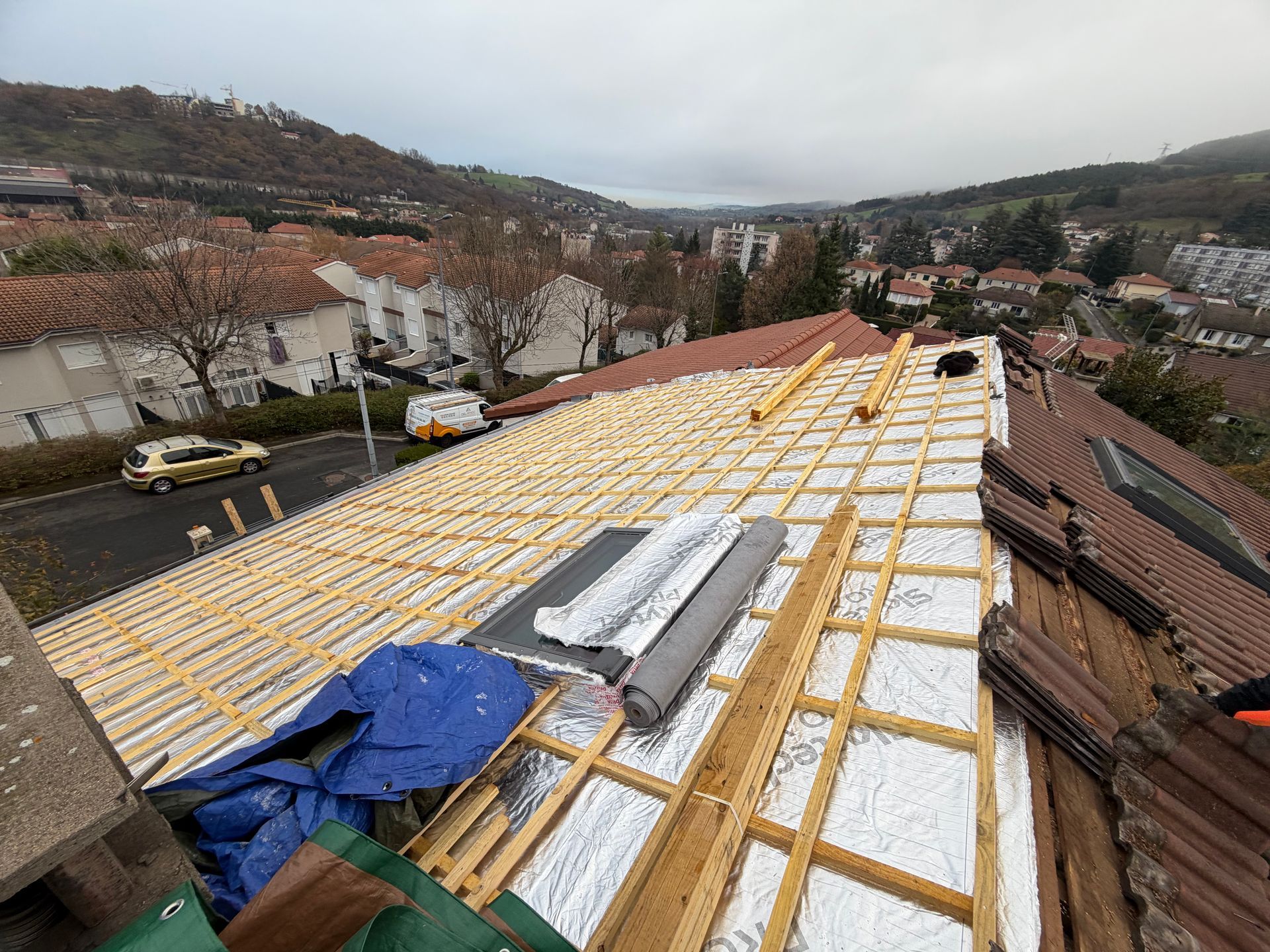 Toiture en construction avec panneaux isolants blancs et charpente en bois jaune dans un quartier de banlieue.