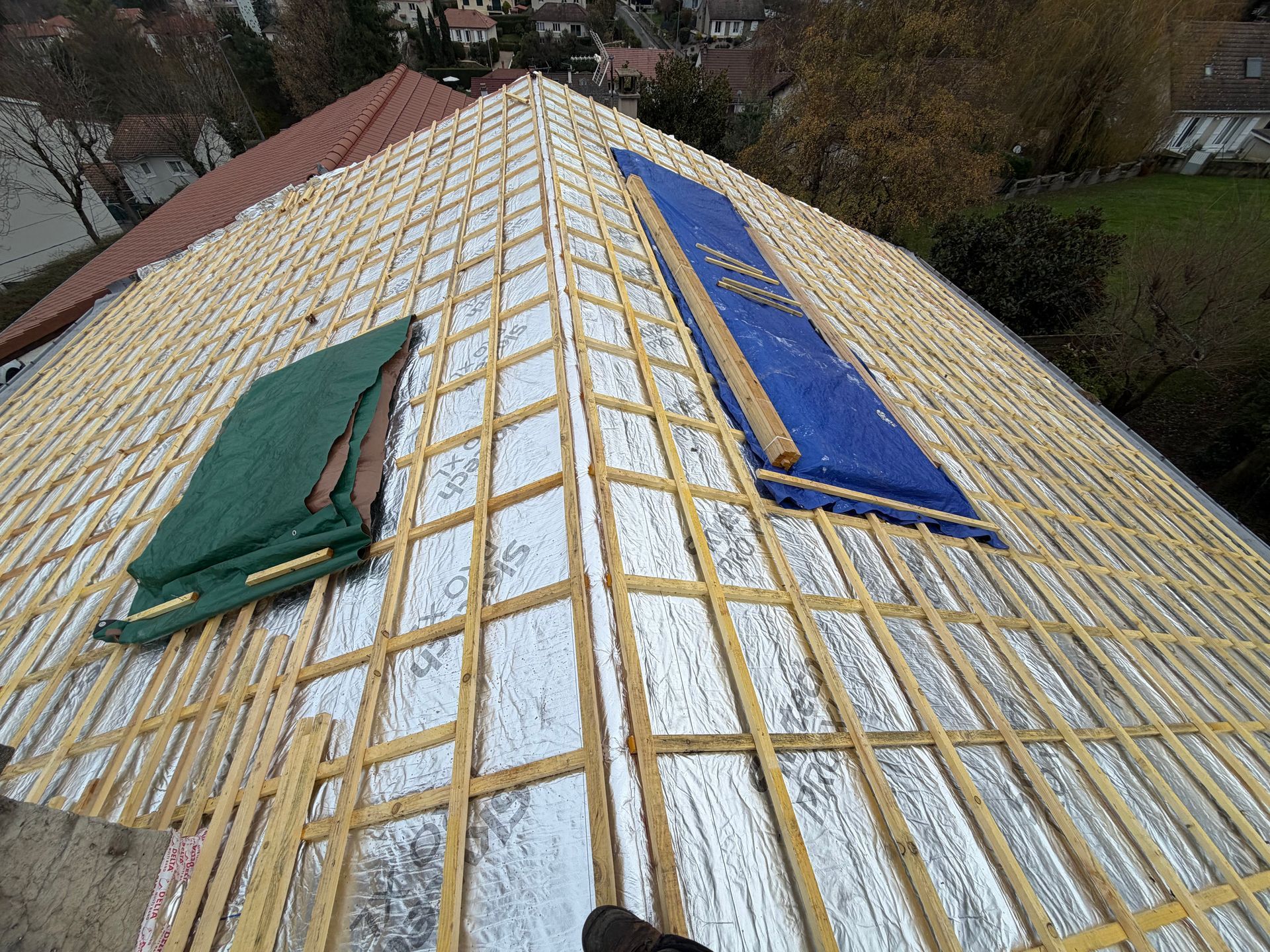 Toiture en construction avec des panneaux isolants blancs et deux bâches bleues et vertes.