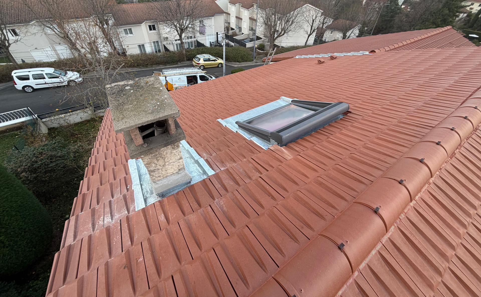 Toit en tuile rouge avec puits de lumière et ouverture de toit, vu d'en haut dans un quartier résidentiel.