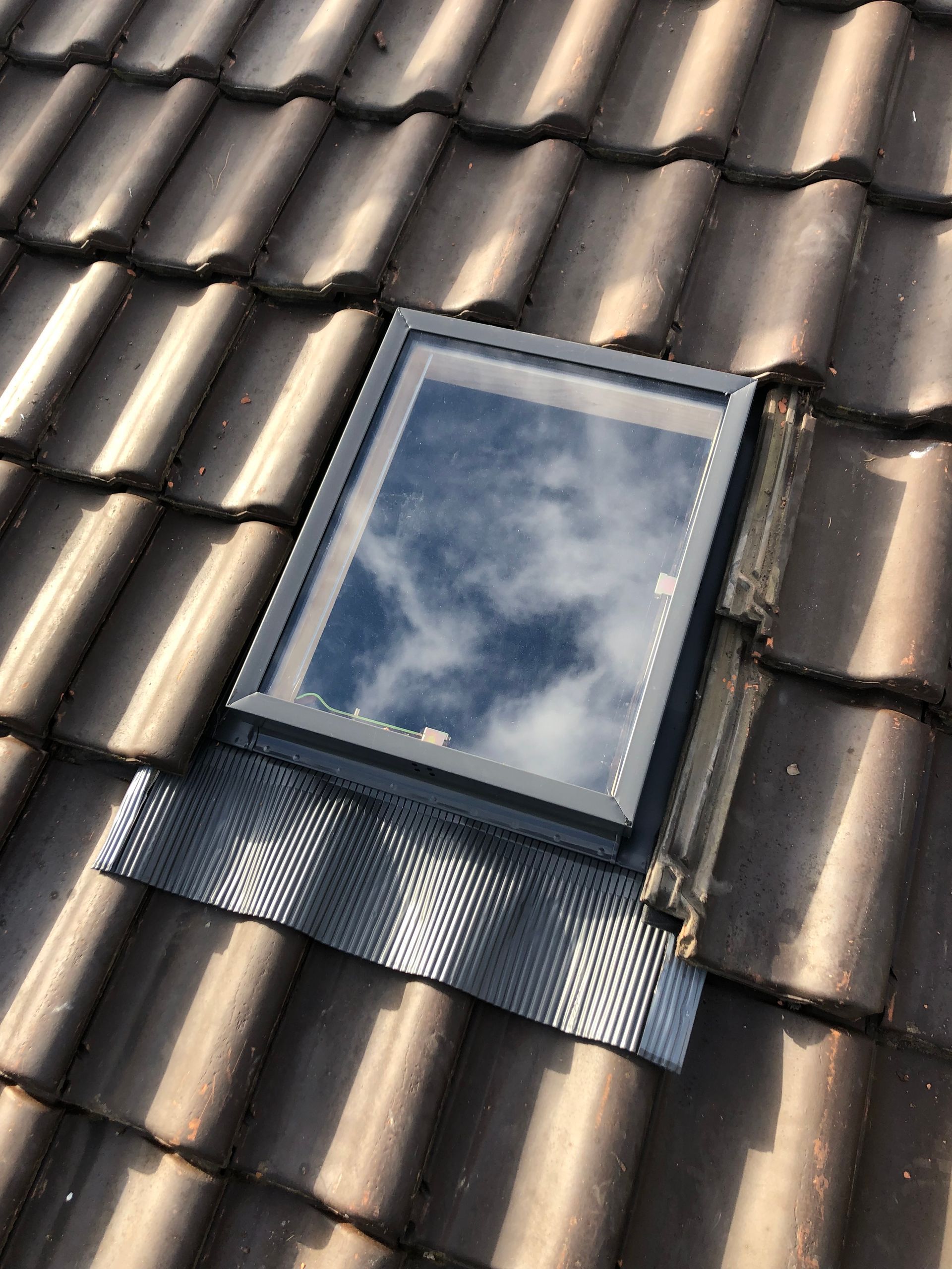 Fenêtre de toit sur un toit de tuiles reflétant les nuages ​​du ciel.