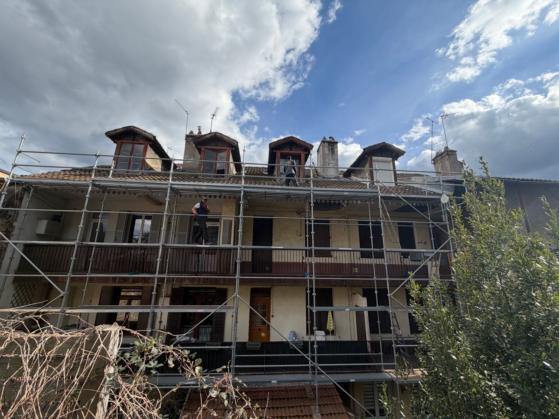 Échafaudages autour d'un immeuble de trois étages en rénovation sous un ciel nuageux.