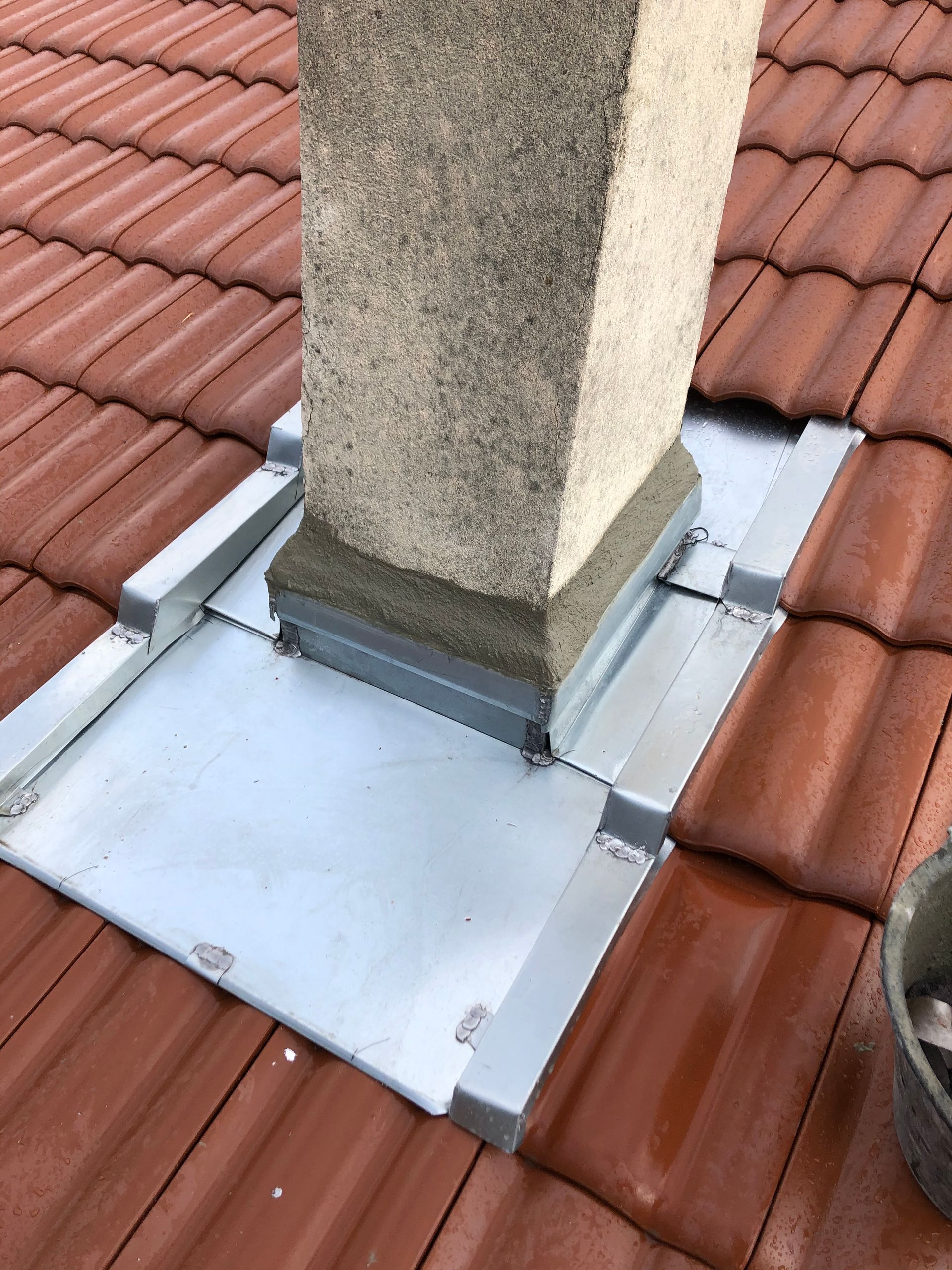 Solin de cheminée sur tuiles en terre cuite rouge avec base en métal blanc et cheminée en stuc gris.