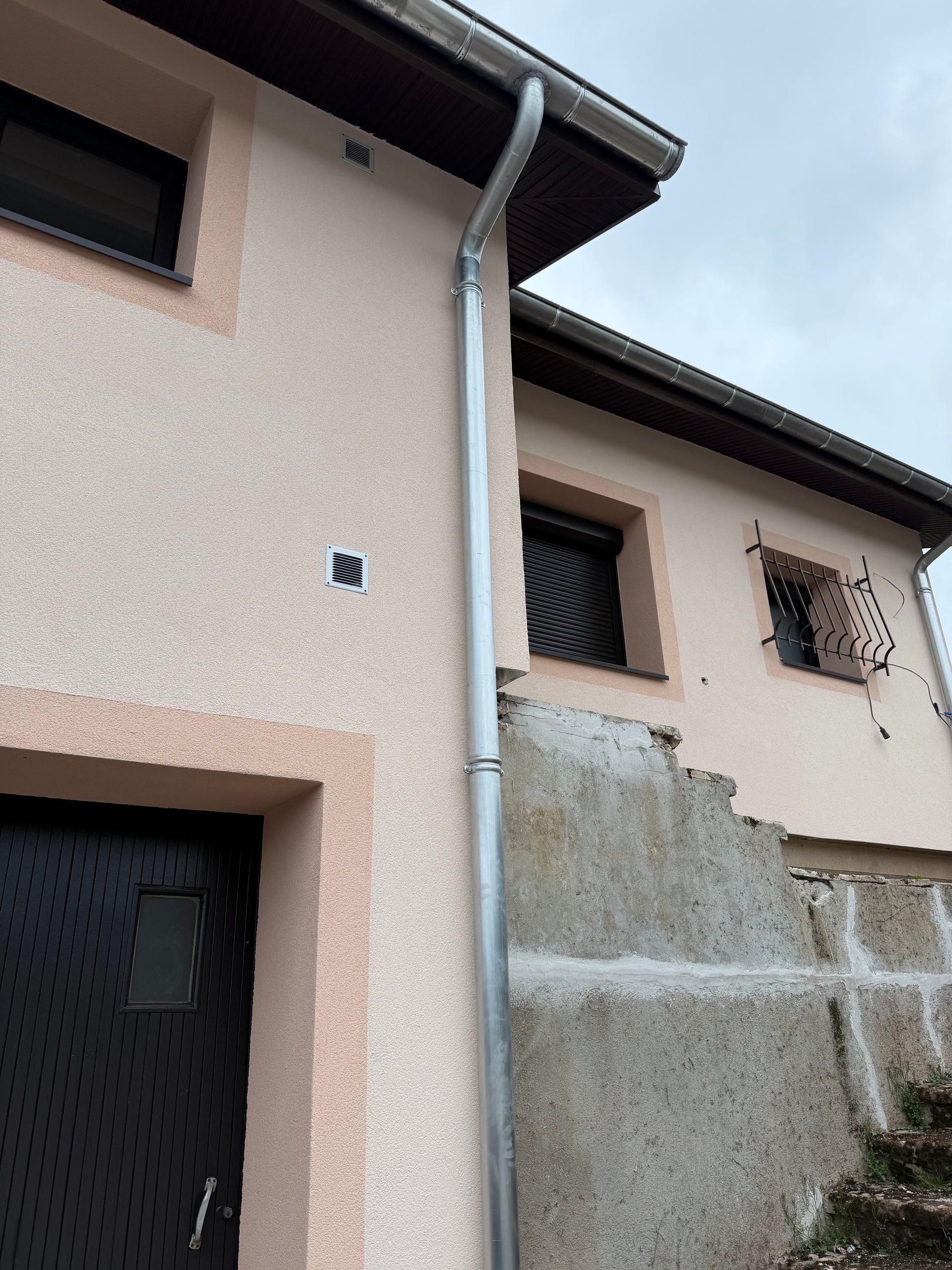 Maisons à deux étages en stuc avec une descente de gouttière grise et un mur de soutènement en béton à l'extérieur.