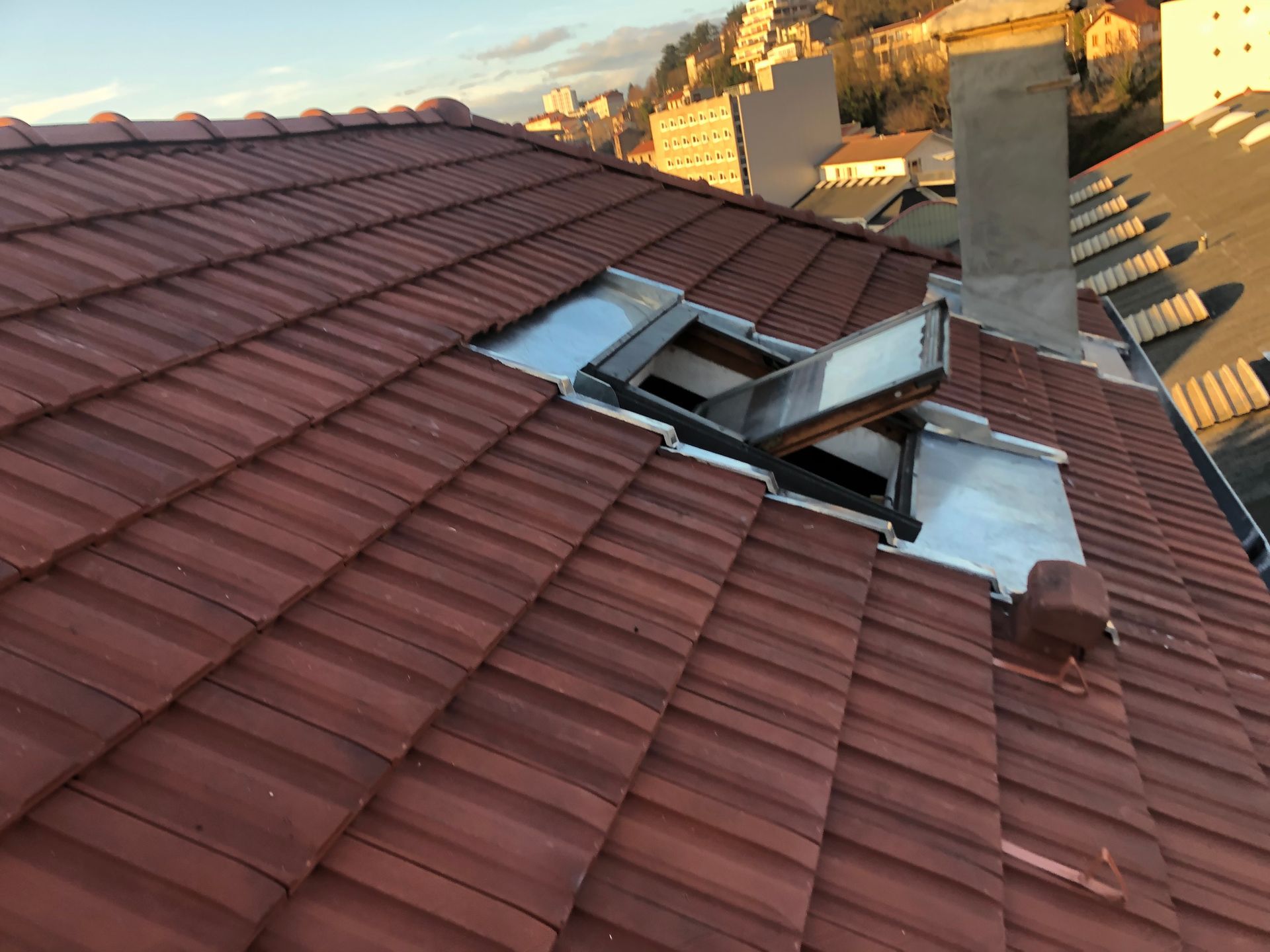 Toiture de tuile rouge endommagée avec une lucarne donnant sur le grenier au-dessus d'un quartier au coucher du soleil