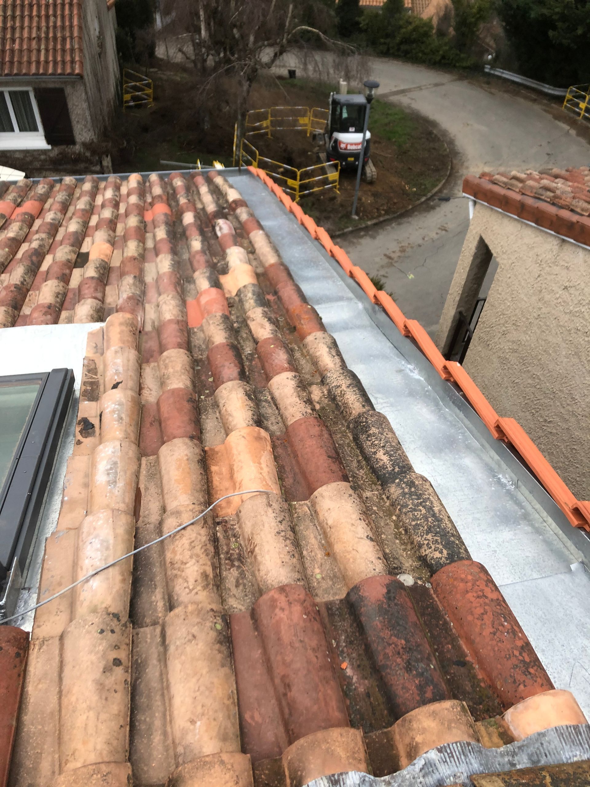 Vue du toit sur des tuiles en terre cuite patinées, à côté d'une allée et des murs de la maison.