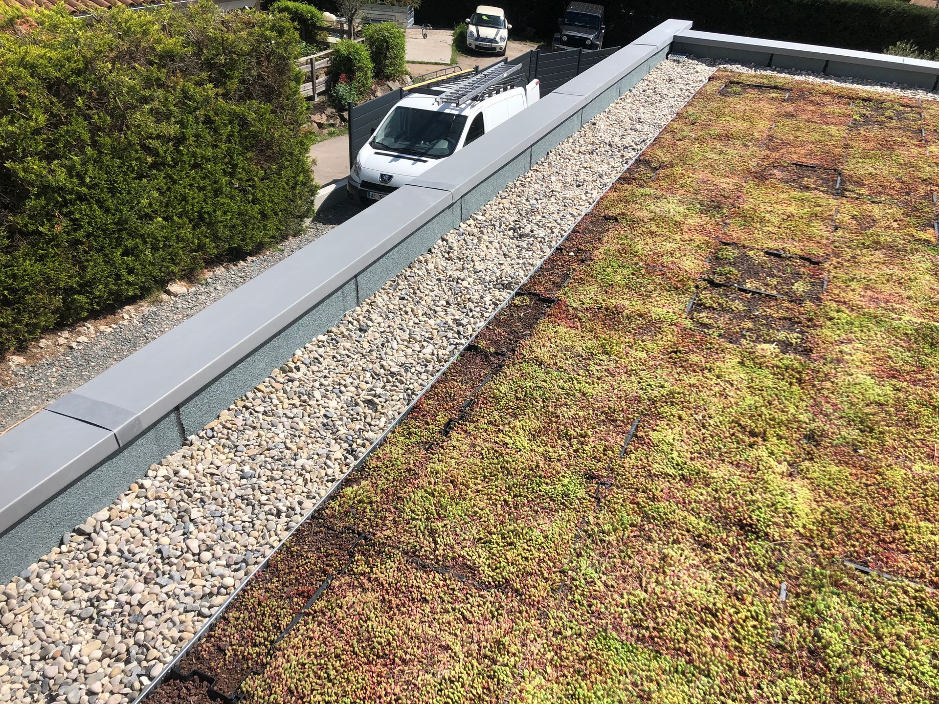 Toit-terrasse végétalisé avec du gravier et la camionnette de l'entreprise garée à côté du bâtiment.