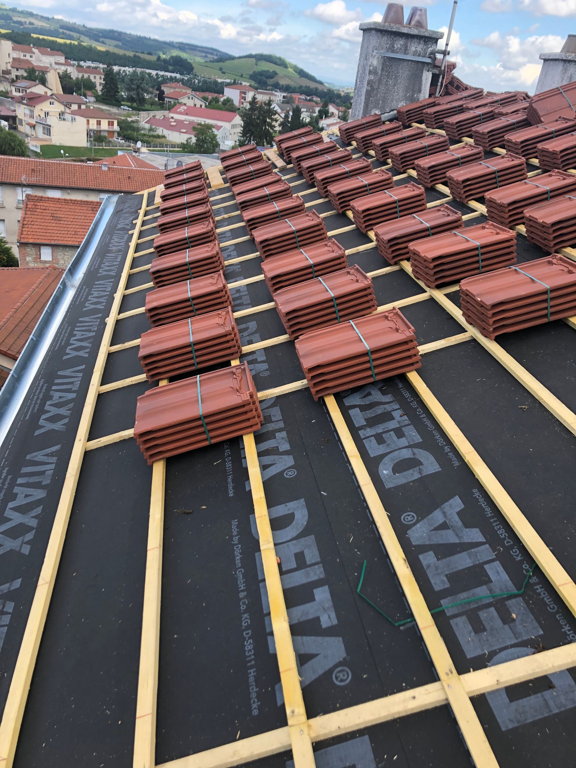 Toiture en construction avec sous-couche noire et rangées de tuiles en terre cuite rouge.