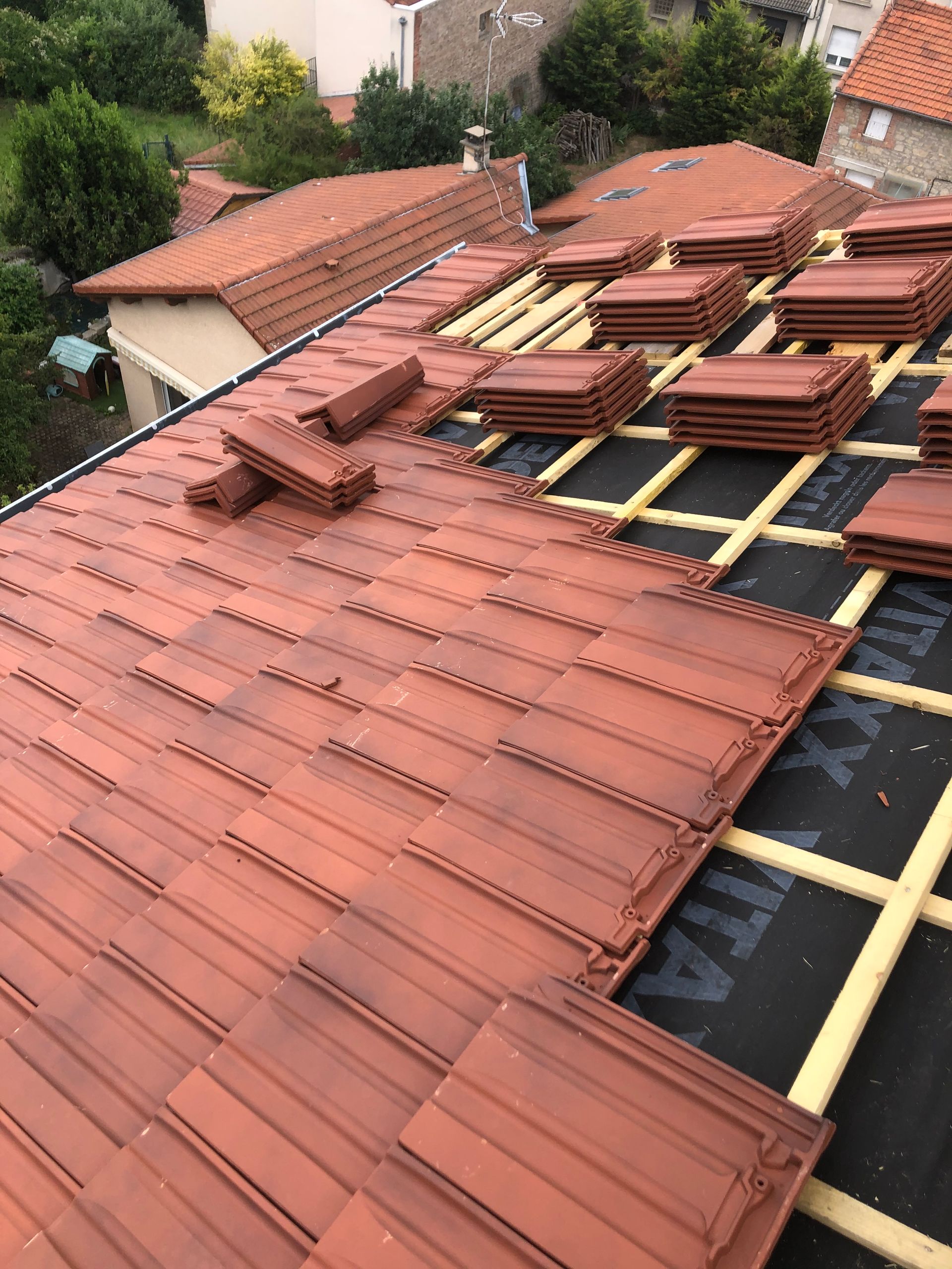 Toiture en réparation avec tuiles rouges empilées et sous-couche noire apparente sur le toit d'une maison.
