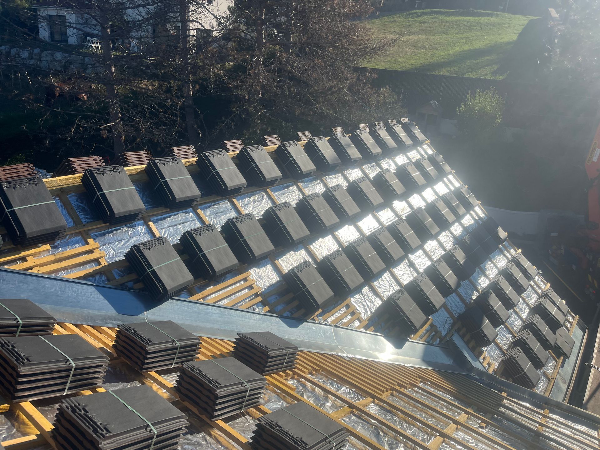 Des rangées de tuiles sombres sur le toit, avec les reflets du soleil et des champs en arrière-plan.