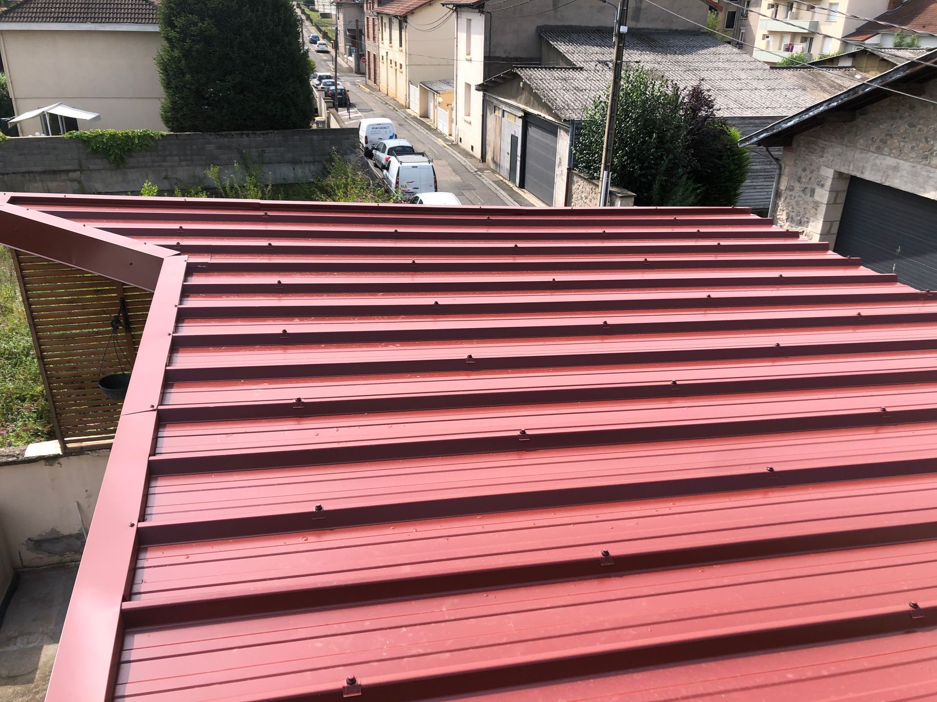Toit en tôle nervurée rouge donnant sur une rue résidentielle et des maisons.