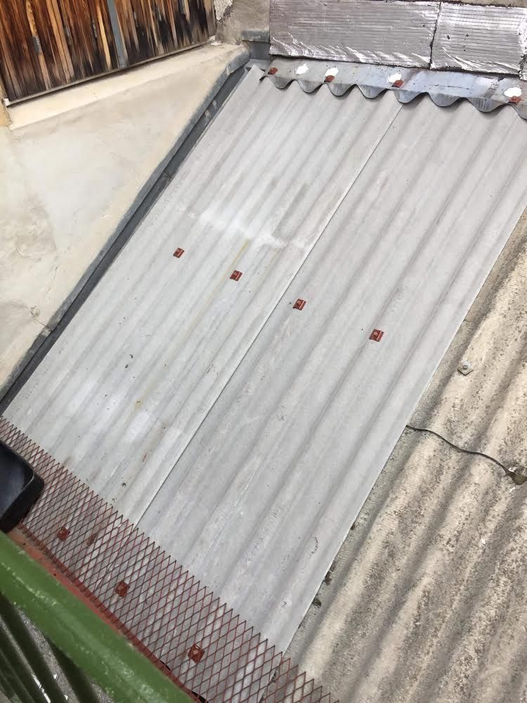 Panneau de toiture ondulé translucide présentant des points de rouille et un bord endommagé sur un toit.