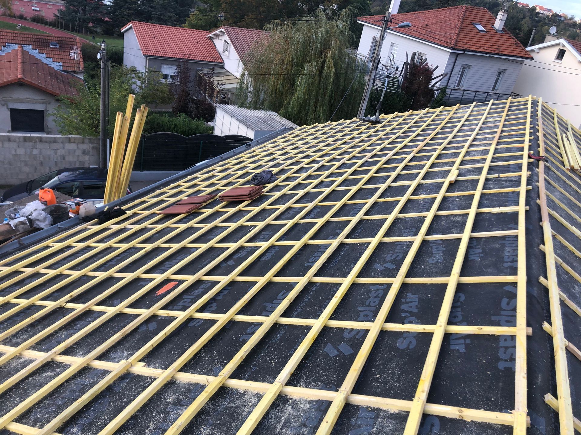 Lattes de toiture jaunes posées sur une sous-couche noire, sur un toit en pente avec des maisons en arrière-plan.