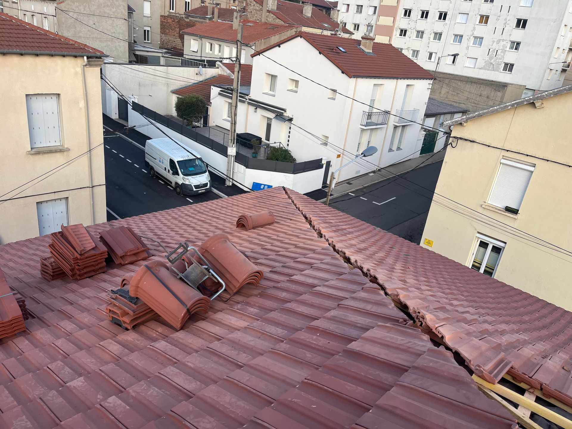 Toiture en tuile rouge avec une crête endommagée donnant sur une rue résidentielle étroite et une camionnette stationnée