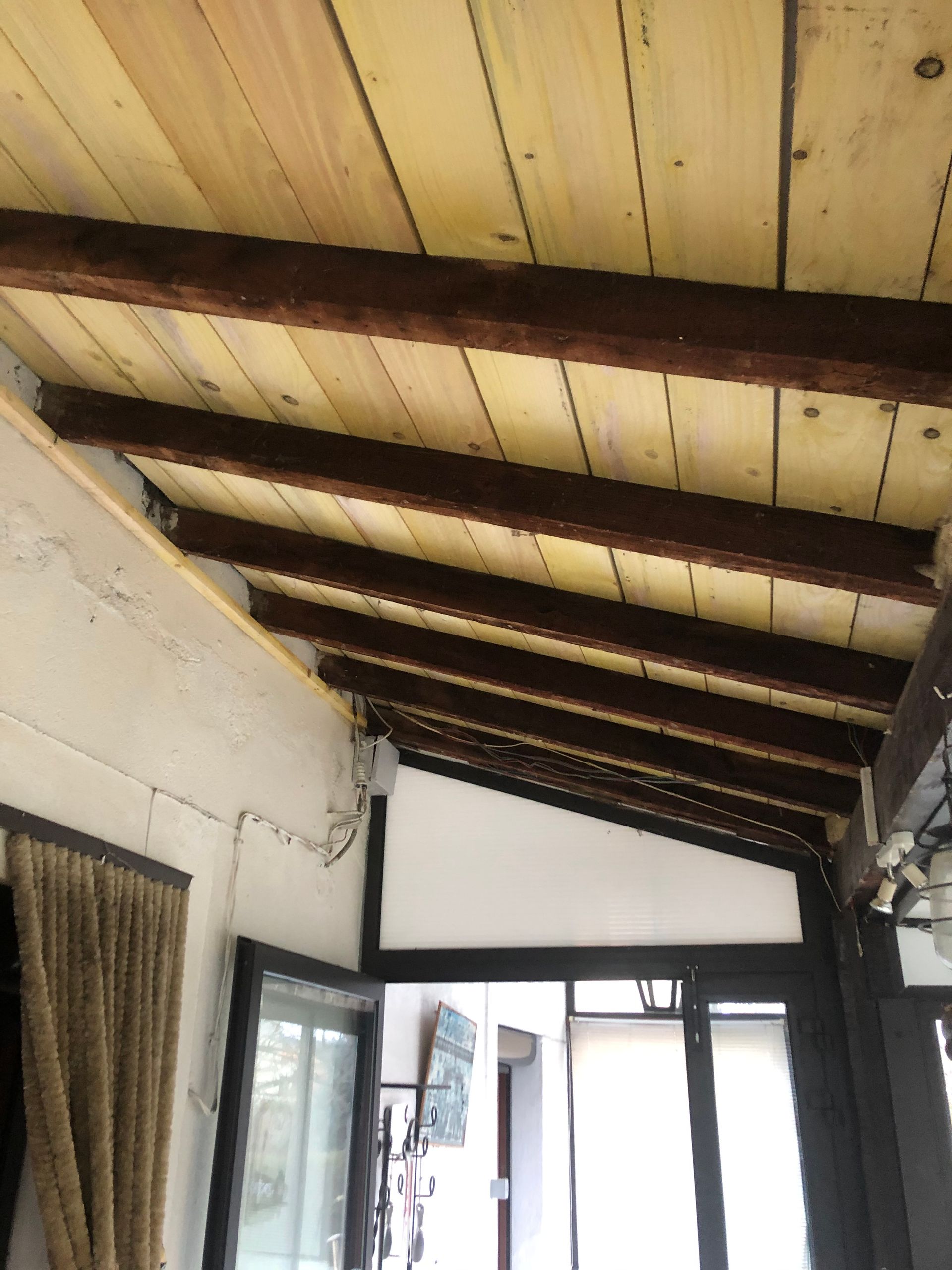 Plafond de véranda couvert avec poutres apparentes sombres et panneaux de bois clair au-dessus d'une porte ouverte.