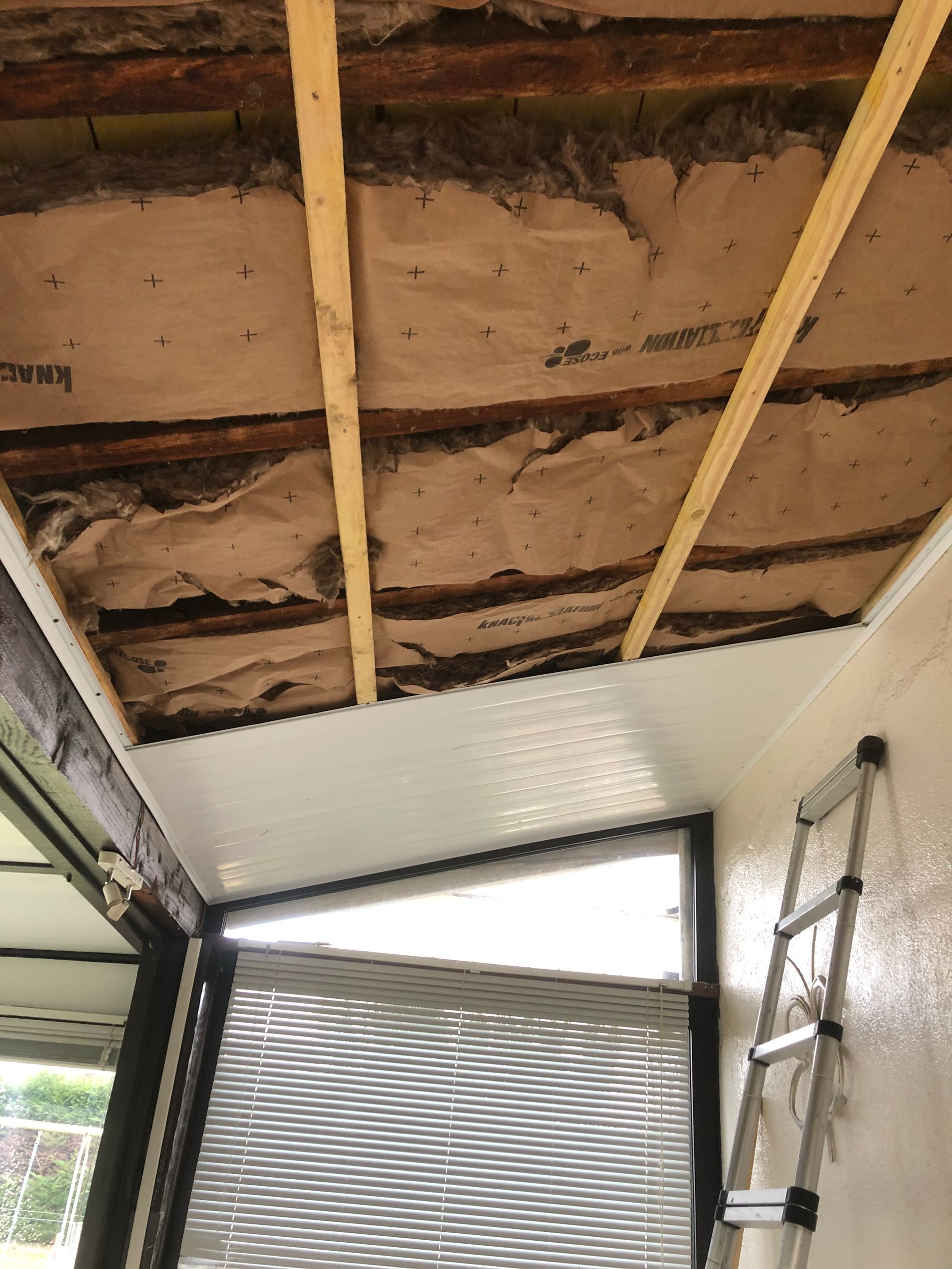 Plafond partiellement apparent avec plâtre endommagé, poutres en bois et échelle à l'intérieur d'une pièce.