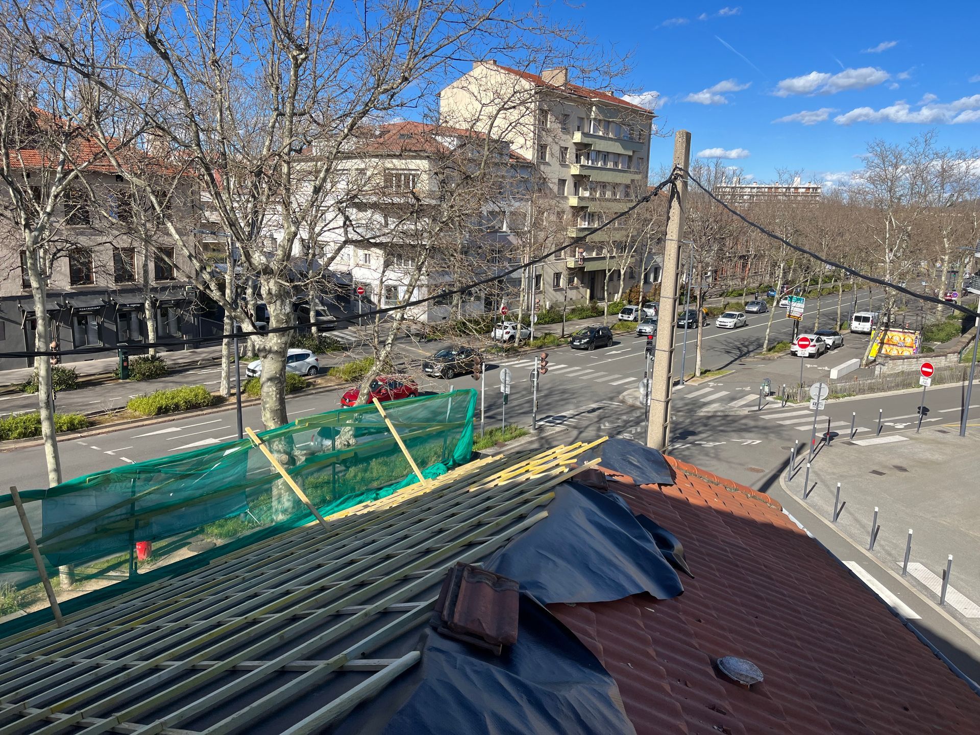 Toit-terrasse recouvert de matériaux de construction, donnant sur une rue, des arbres et des immeubles d'habitation par temps clair.