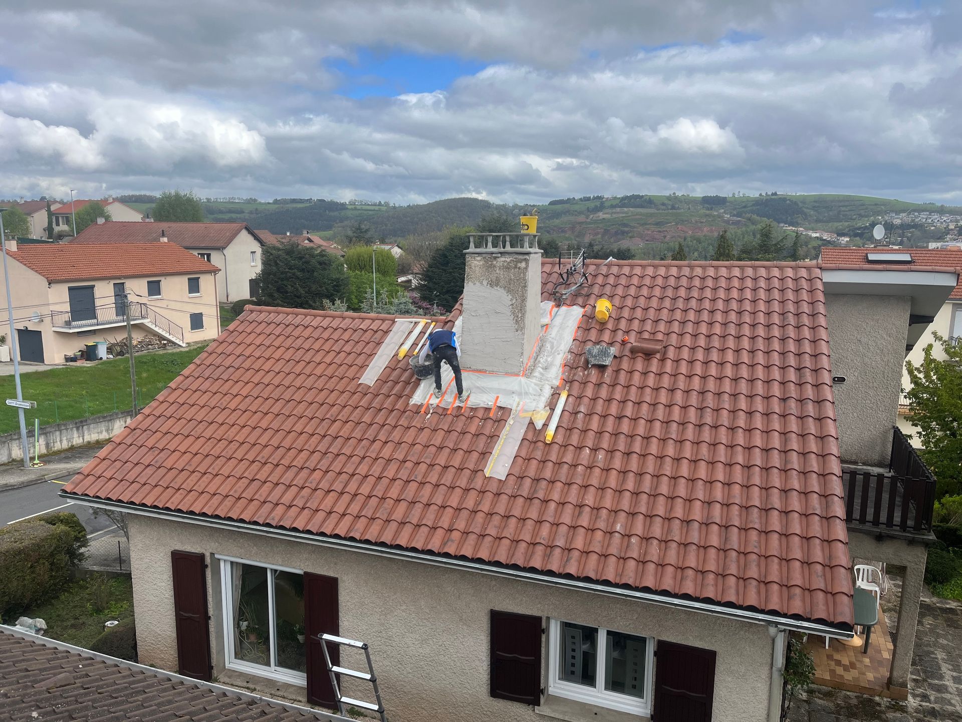 Maison au toit de tuiles rouges, cheminée en cours de réparation, vue d'en haut dans un quartier rural.