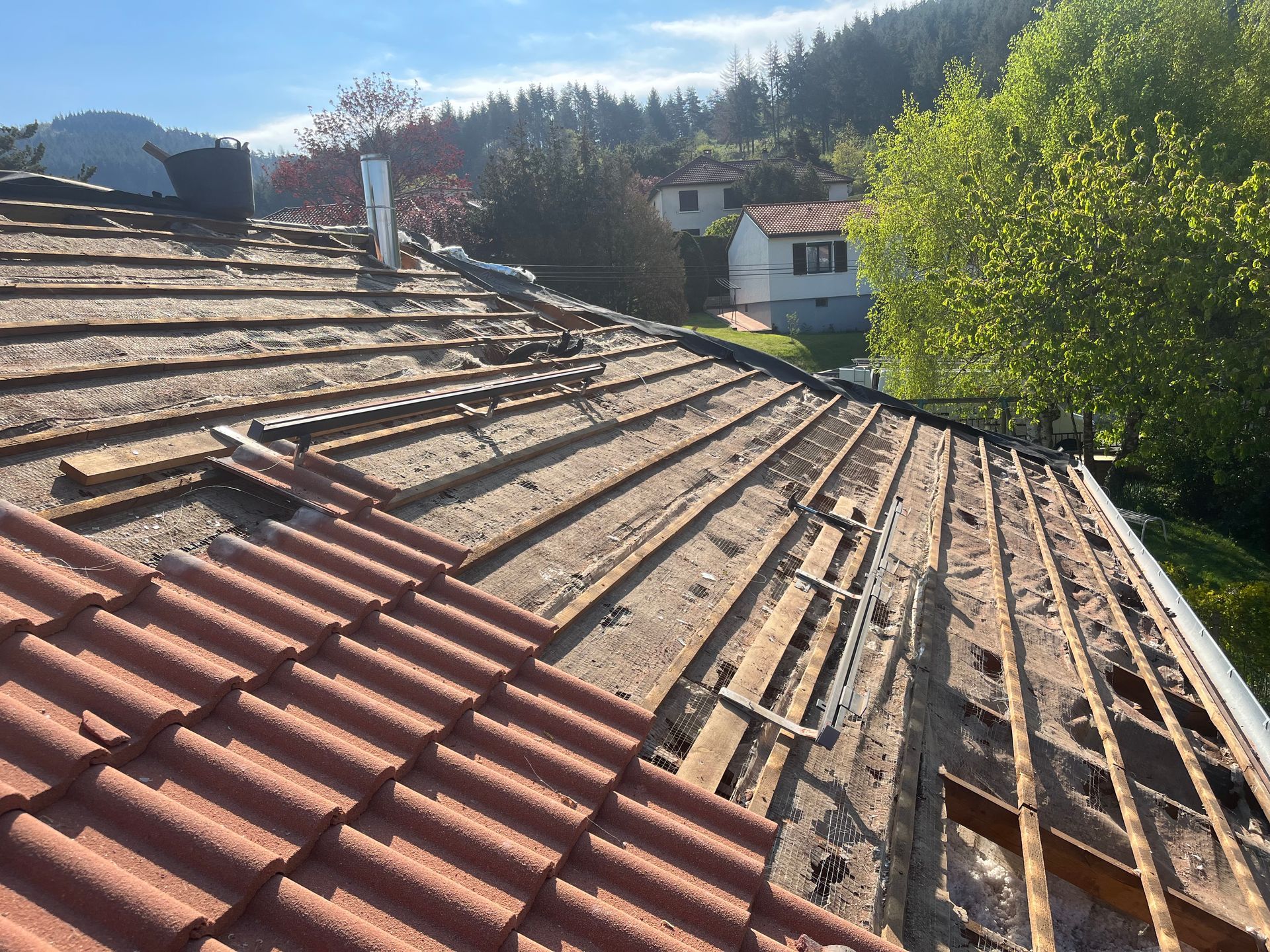 Maison partiellement rénovée avec charpente apparente en bois et tuiles rouges sous un ciel ensoleillé.