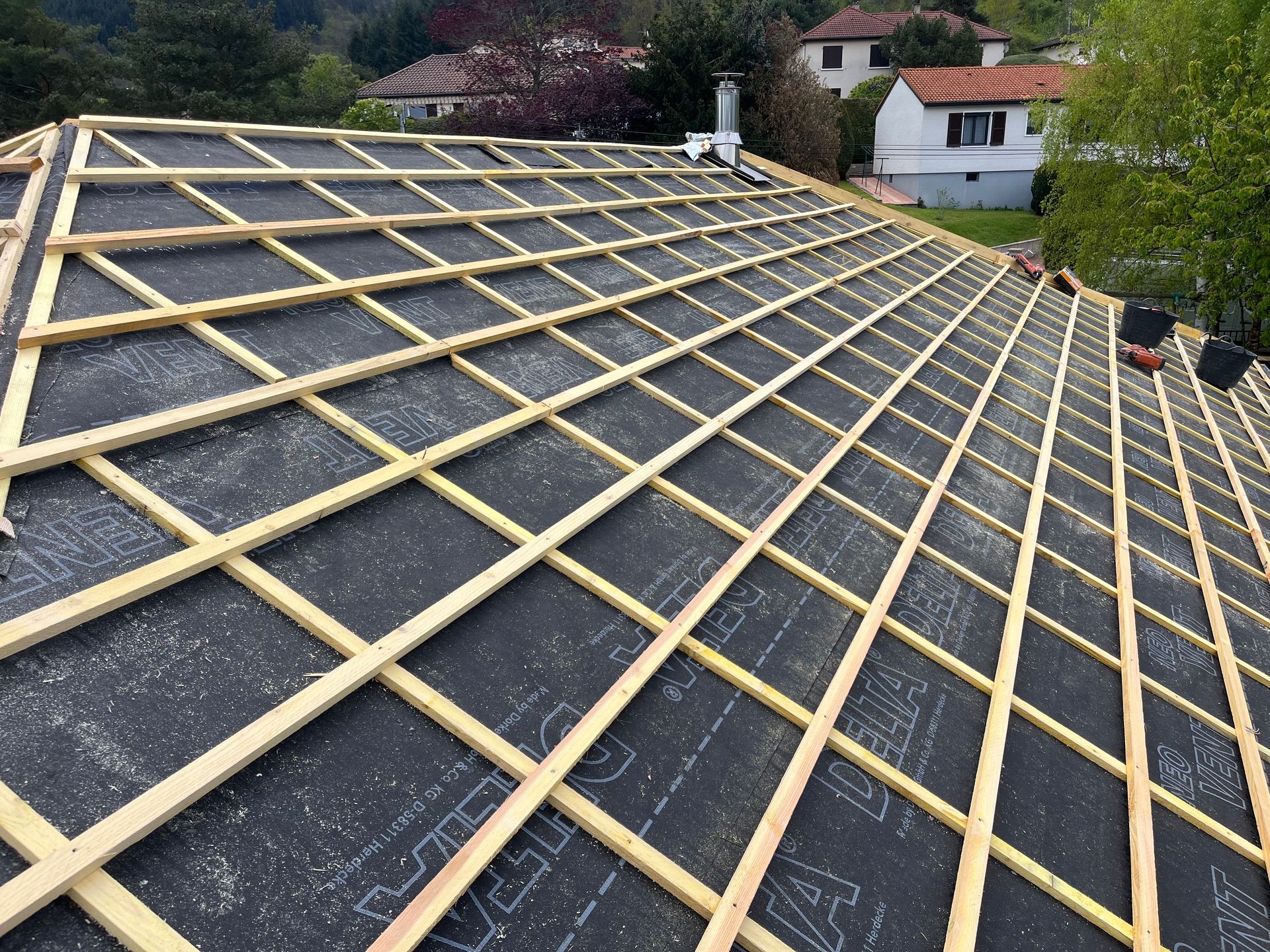 Toiture en réparation avec liteaux de bois posés sur un feutre bitumé foncé, vue de dessus.