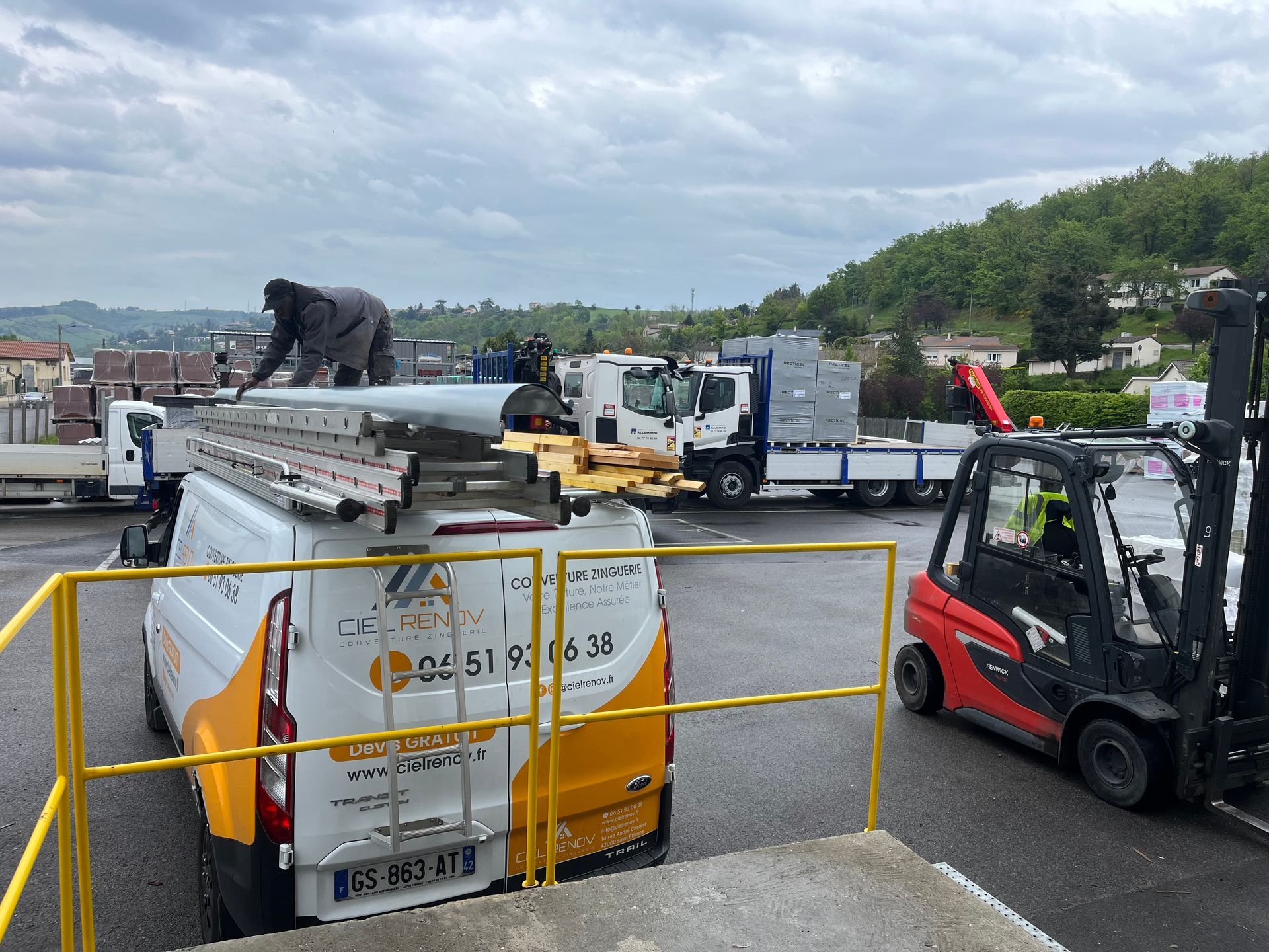 Camionnette de l'entreprise à côté d'un chariot élévateur sur un chantier de construction sous un ciel nuageux.