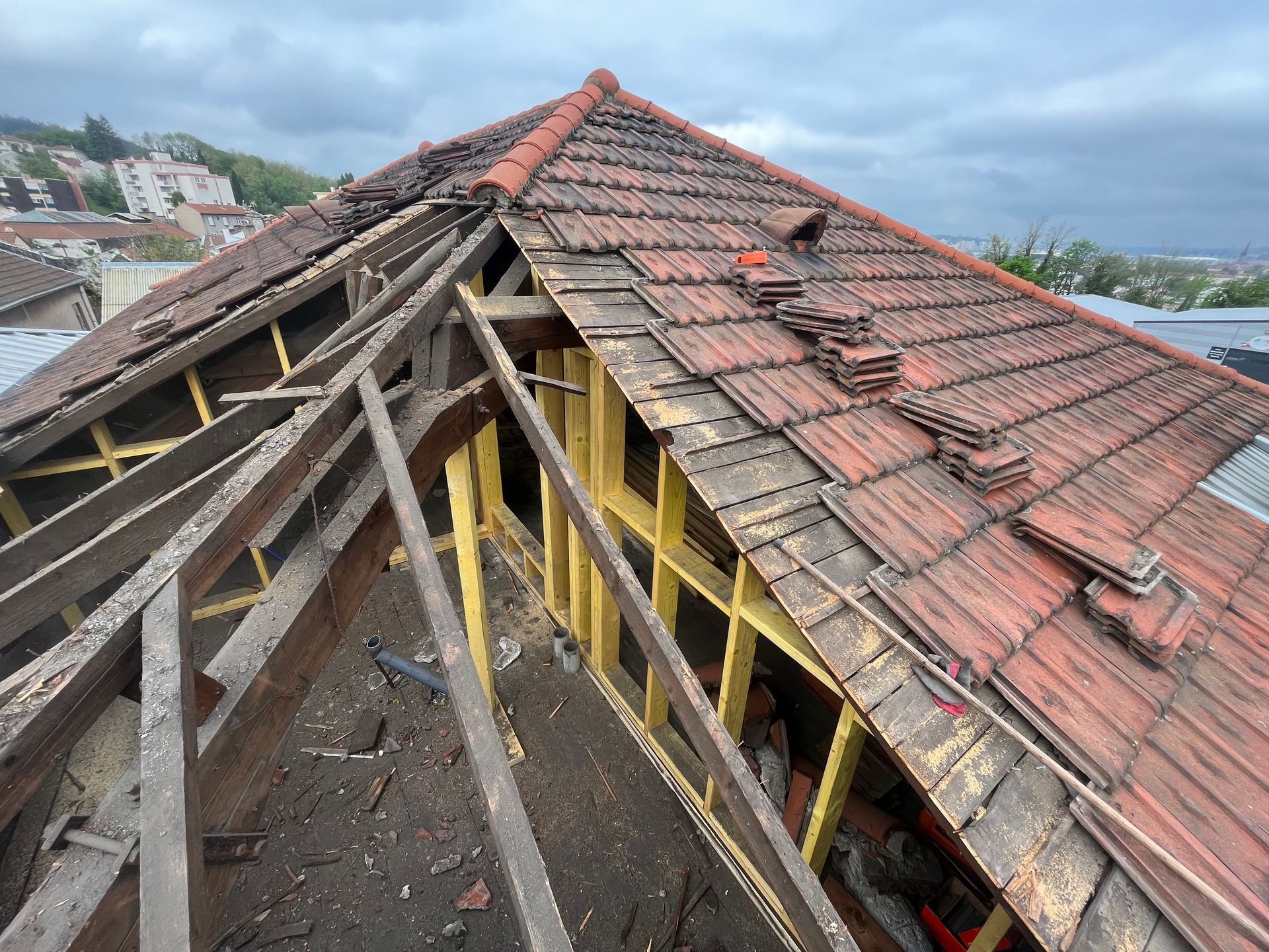 Vue aérienne du toit d'un bâtiment en construction, montrant la charpente en bois apparente et les tuiles en terre cuite non fixées.