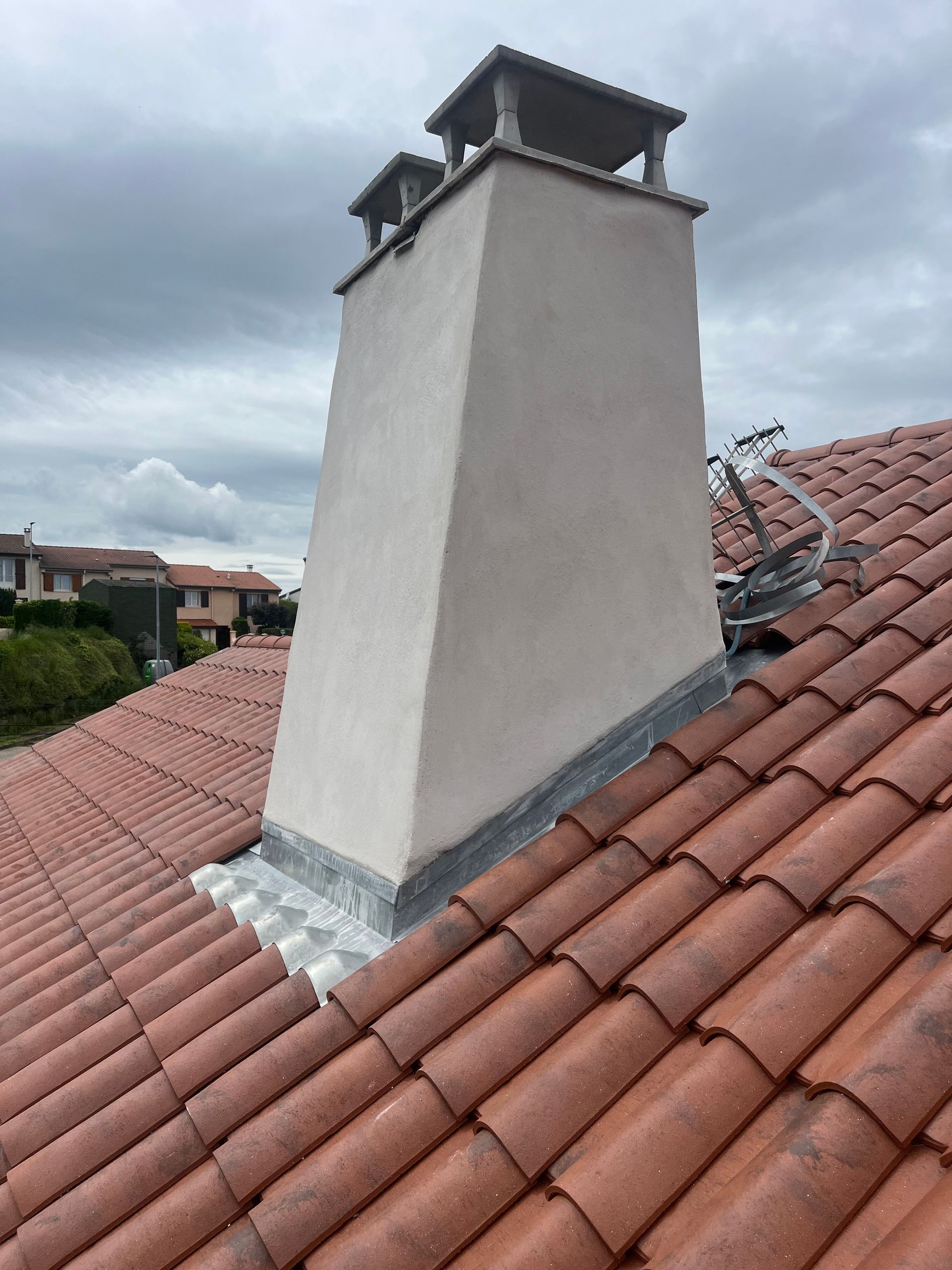Toit de tuiles avec une cheminée blanche sous un ciel nuageux.