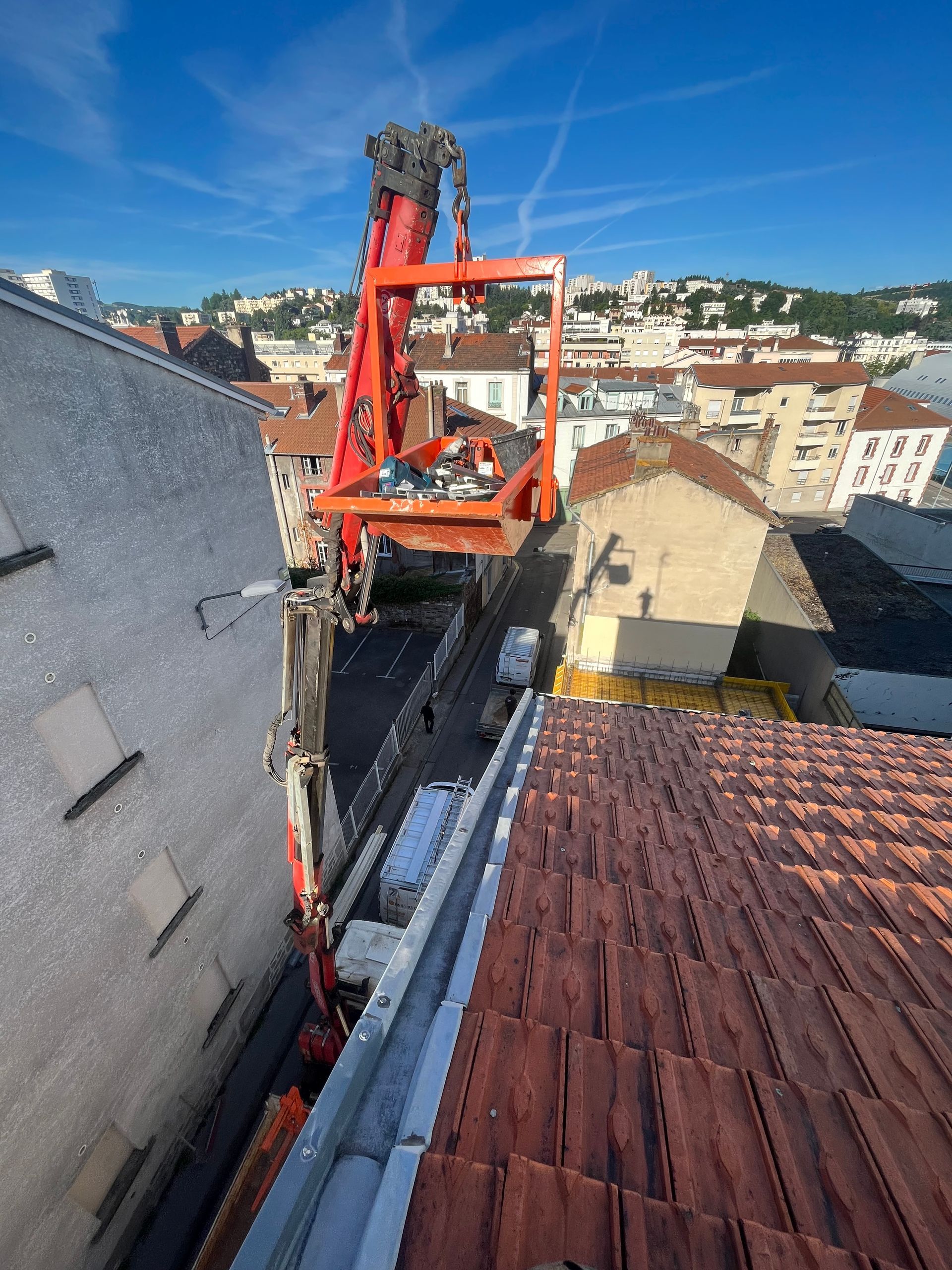 Un monte-charge rouge sur le toit soulève un ouvrier à côté d'un bâtiment sous un ciel bleu.