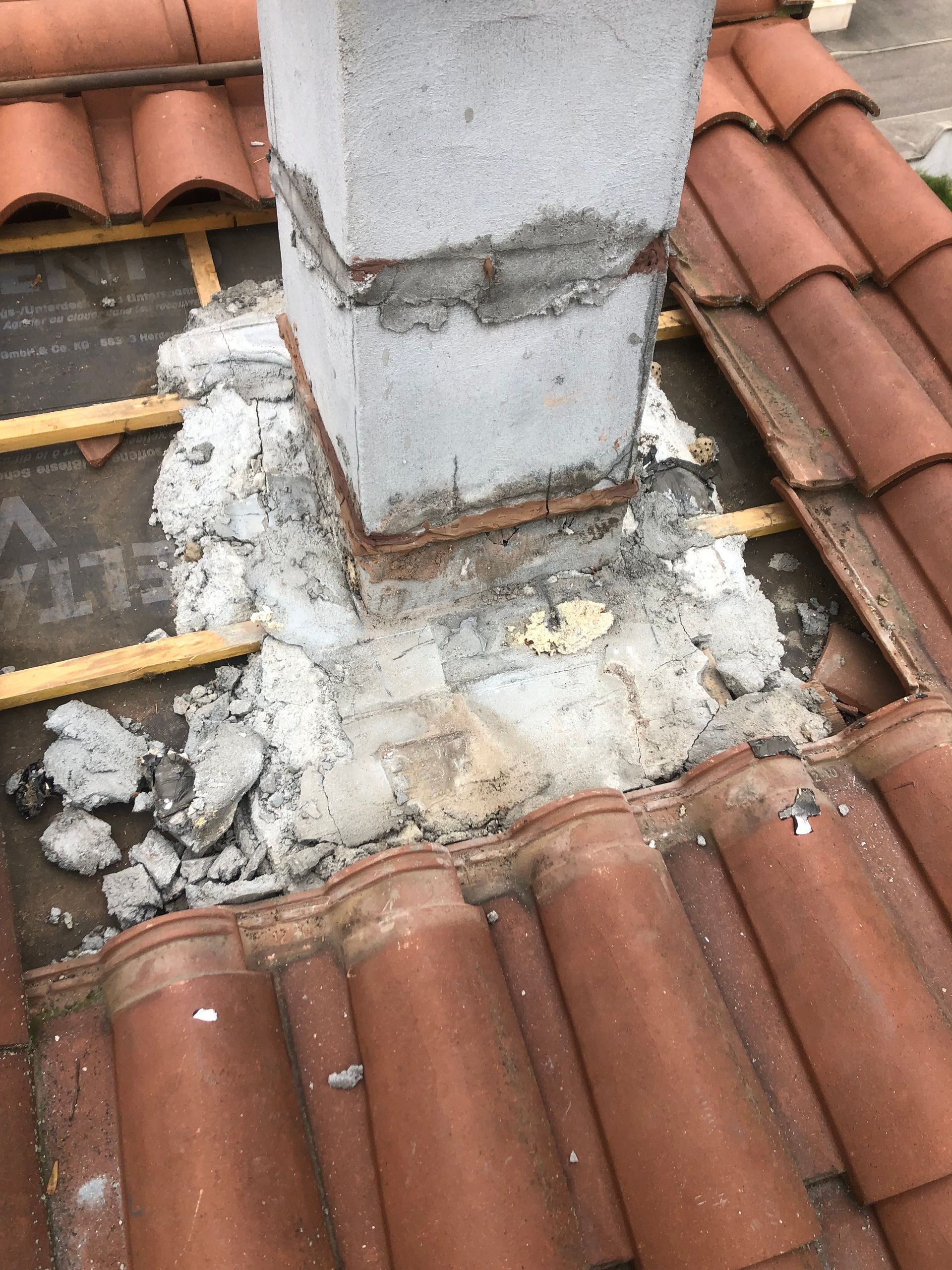 Une cheminée sur un toit de tuile, avec du mortier de béton apparent et irrégulier à sa base, là où elle rejoint le matériau de couverture.