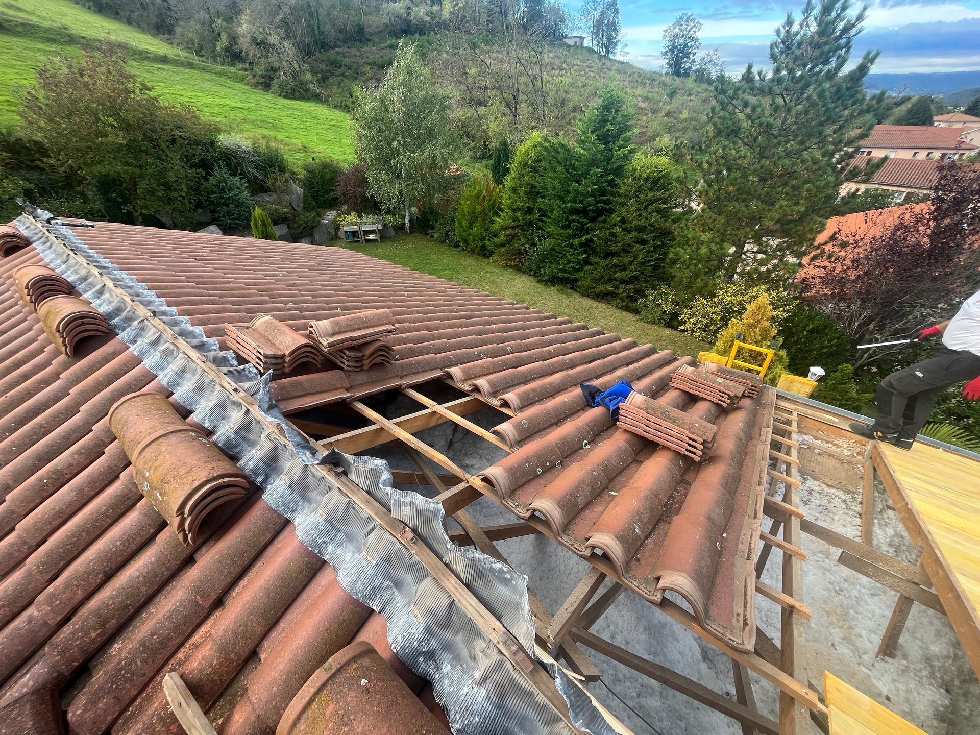 Allée résidentielle longeant une maison en pierre avec des voitures garées sous un ciel bleu clair.