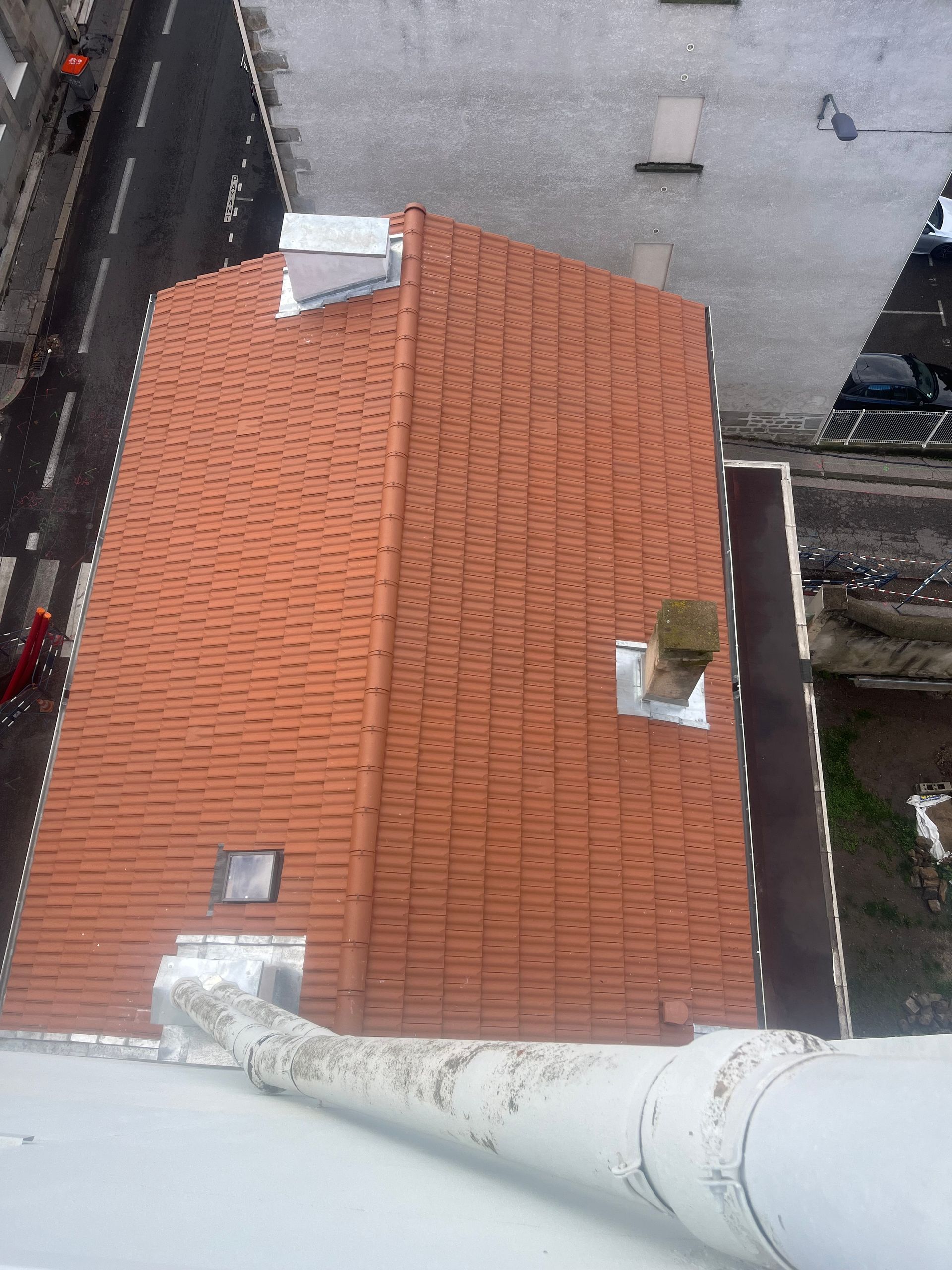 Vue aérienne d'un toit de tuile rouge jouxtant un bâtiment gris et une rue étroite.