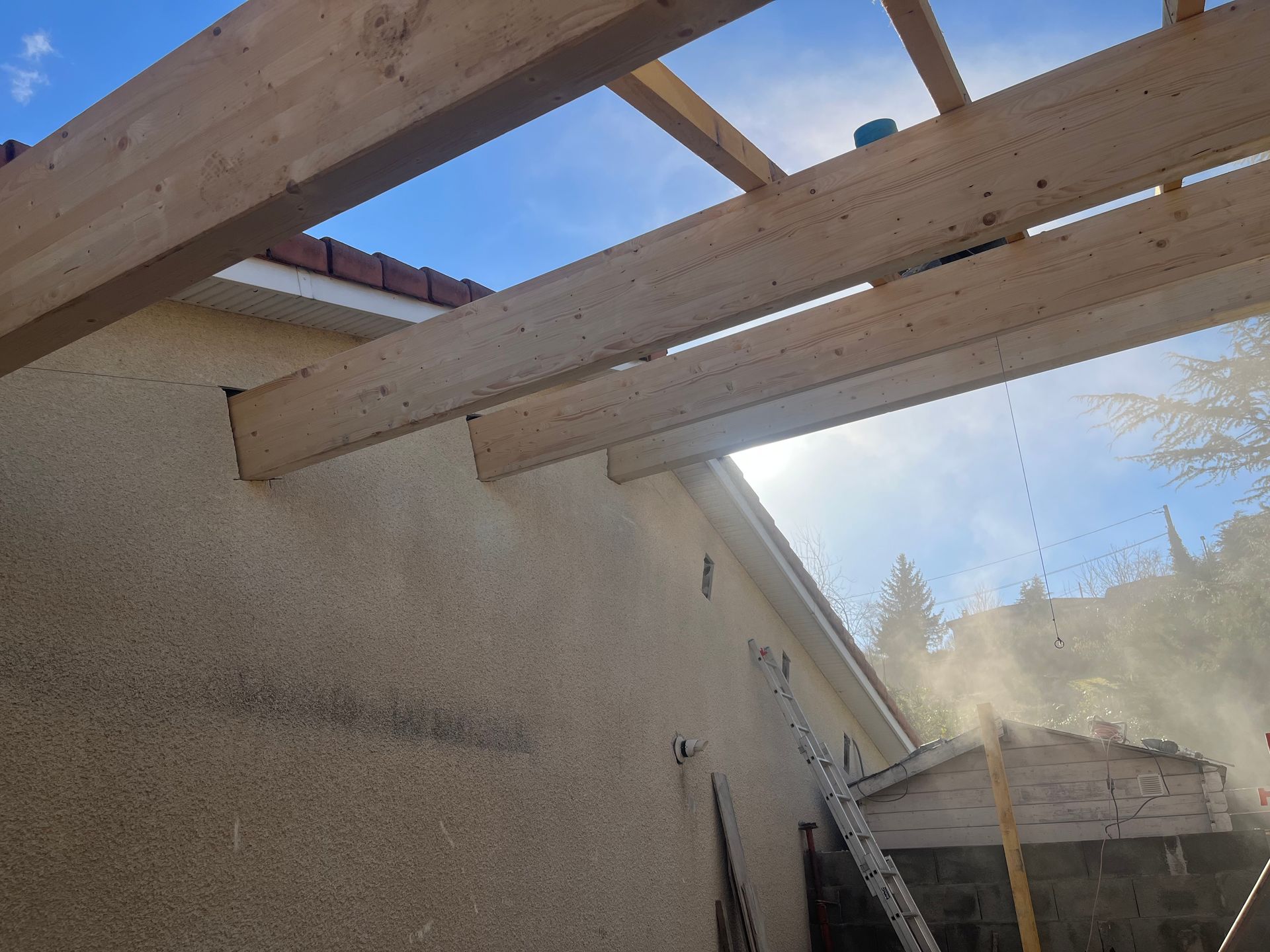 Toiture ouverte au-dessus d'un mur beige, avec un ciel bleu et de la poussière ou de la brume en arrière-plan.