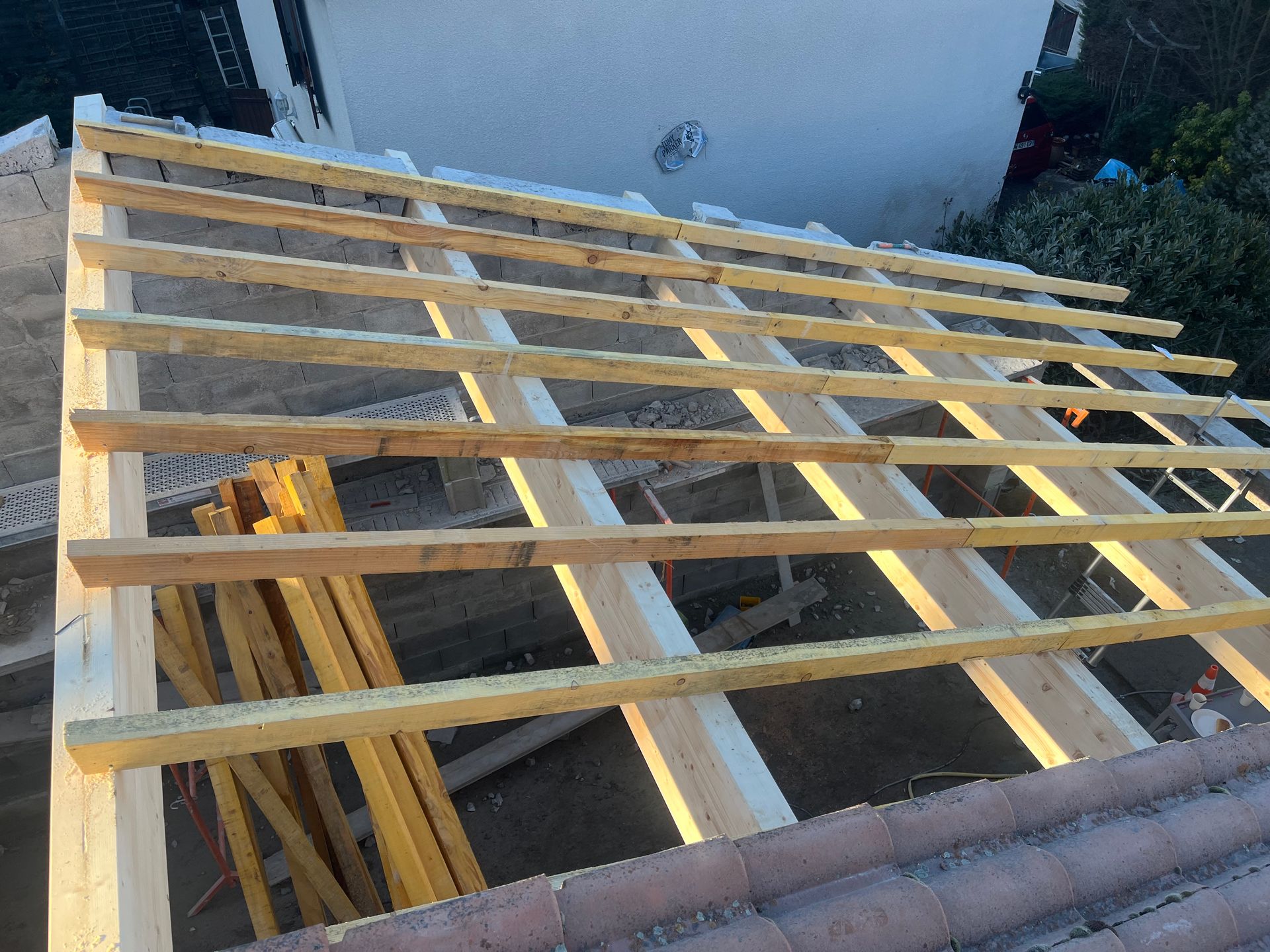 Une charpente de toit en bois partiellement construite, avec des chevrons installés au-dessus d'un bâtiment en construction.