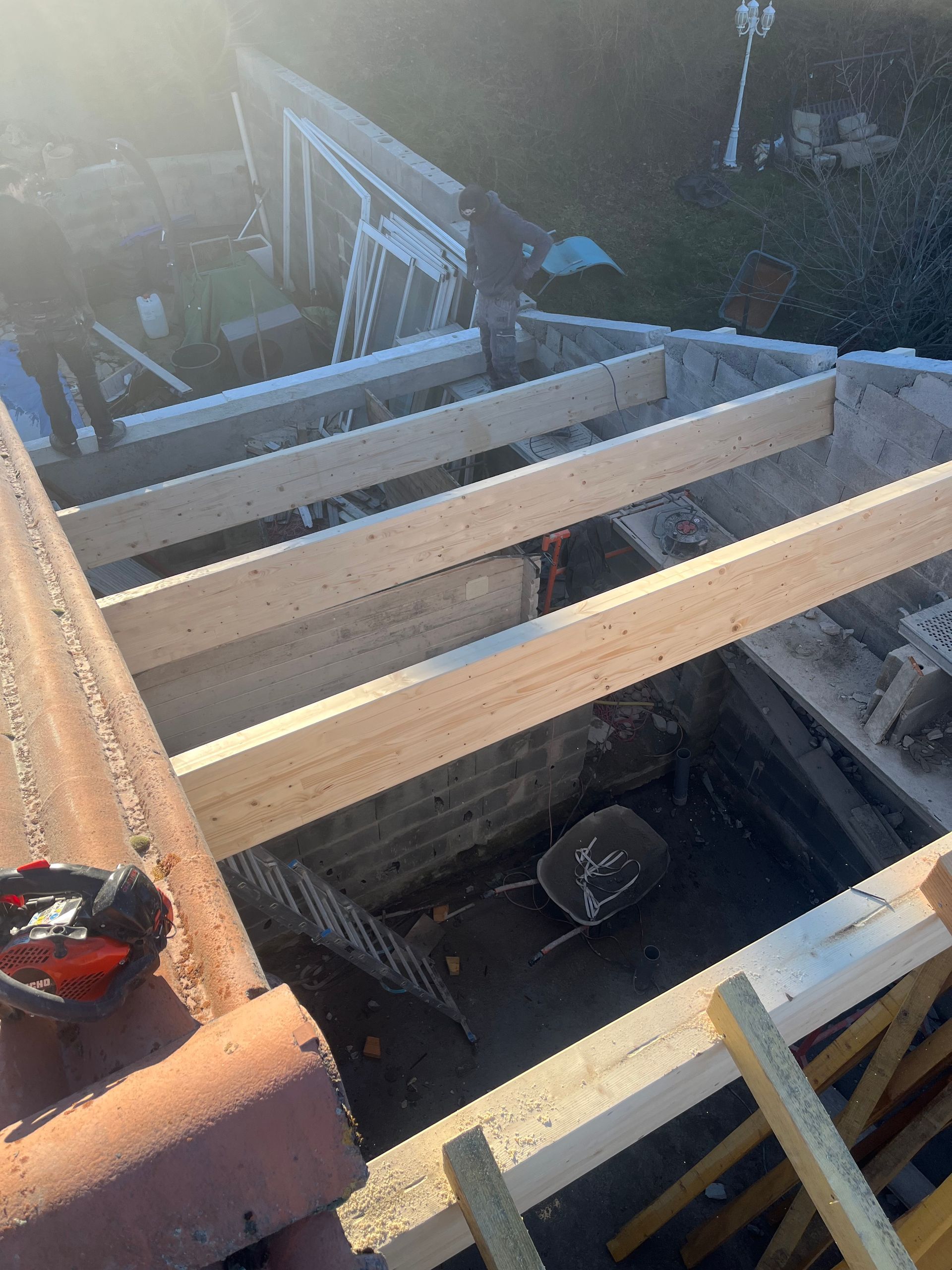 Vue aérienne d'une charpente de toit en bois avec poutres et échelle sur un chantier de construction.