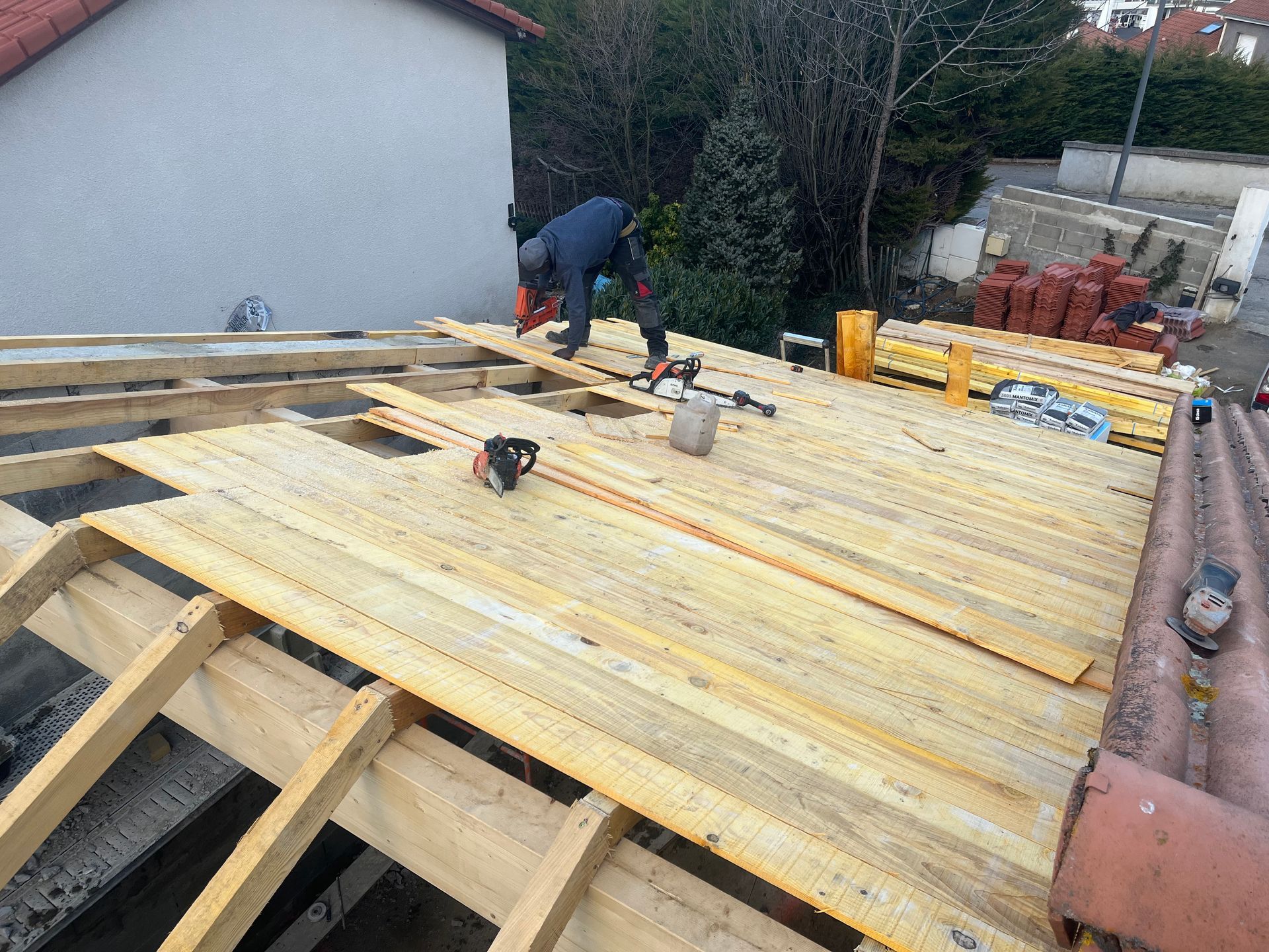 Une personne travaille sur une charpente de toit en bois, posant des planches à l'extérieur.