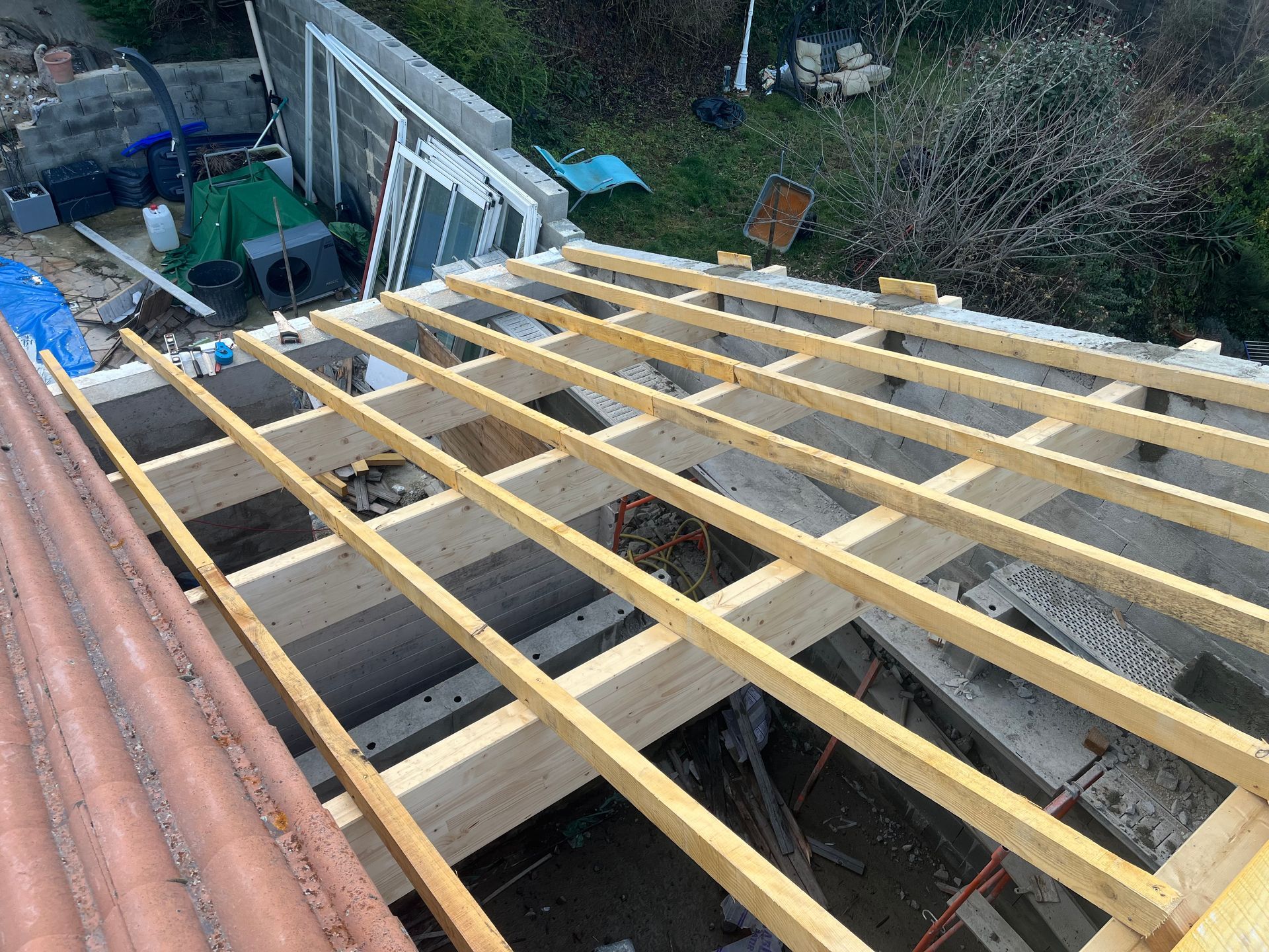 Poutres de toit en bois en cours de construction sur une charpente extérieure, avec des échafaudages et des débris à proximité