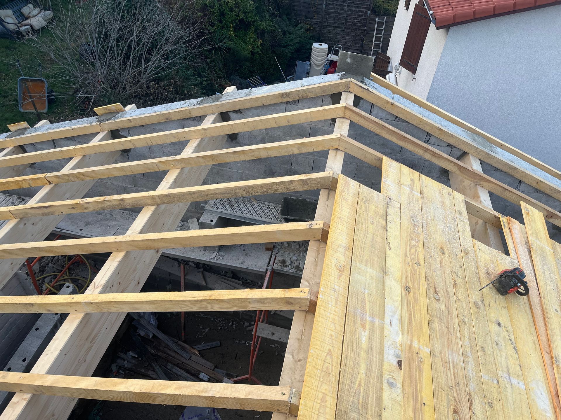 Un toit en construction avec des chevrons en bois installés et partiellement recouverts de panneaux de bois.
