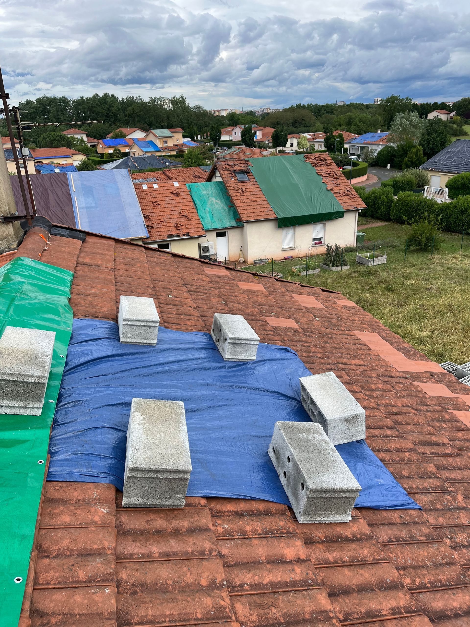 Bâches sur les toits et parpaings dans un village, sous un ciel nuageux, avec des maisons en arrière-plan.