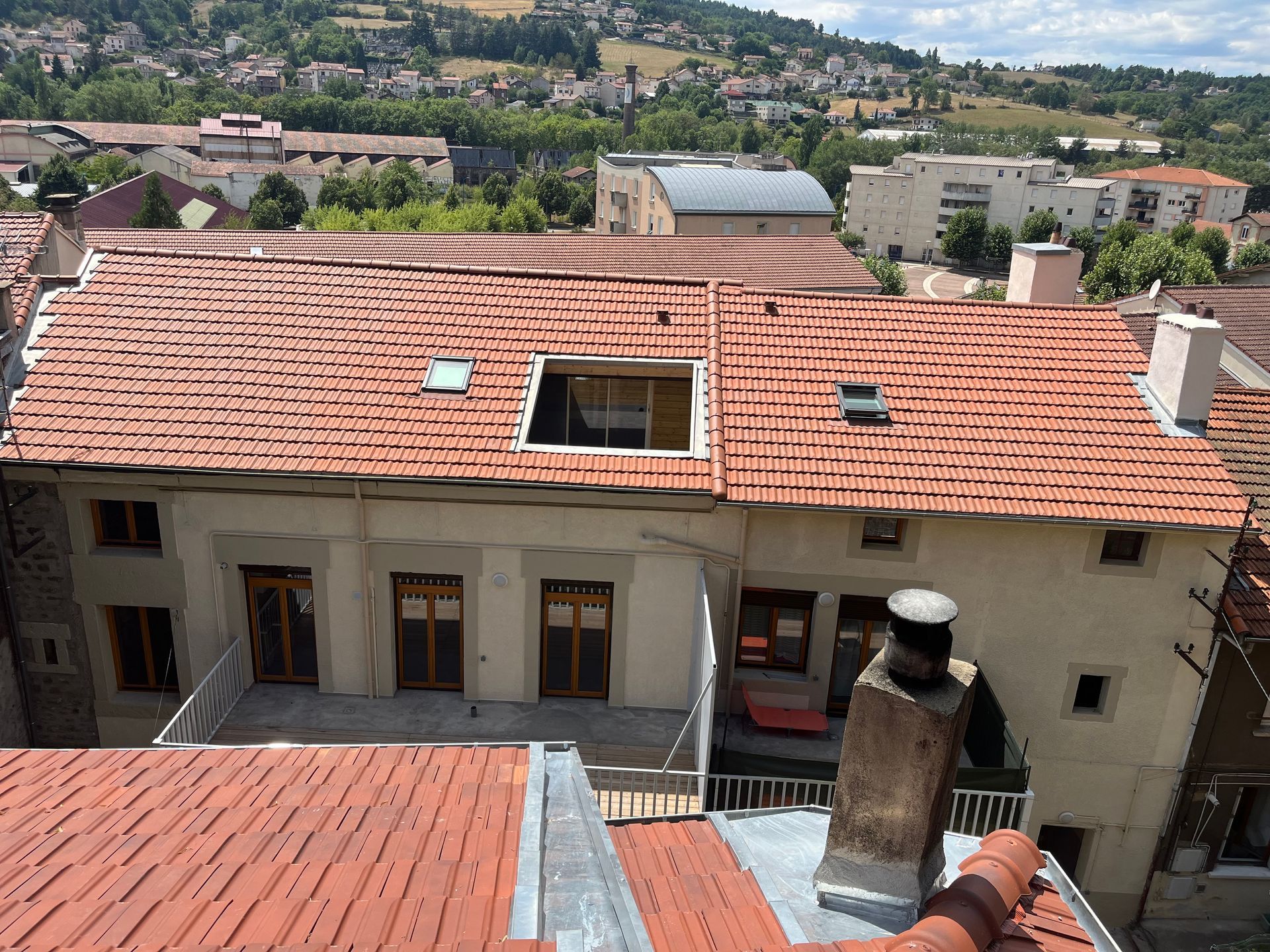 Toit avec des toits de tuiles rouges et des cheminées donnant sur une ville à flanc de colline en arrière-plan.