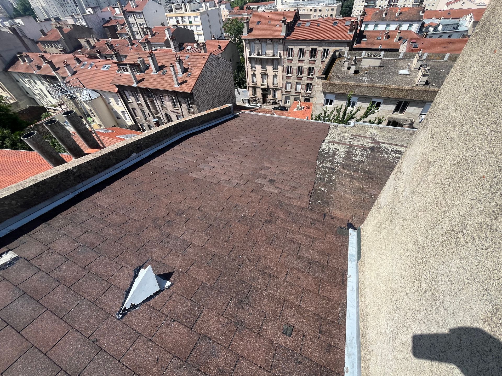 Vue depuis un toit sur des bâtiments aux tuiles rouges et une façade en pierre au loin, dans une ville historique.