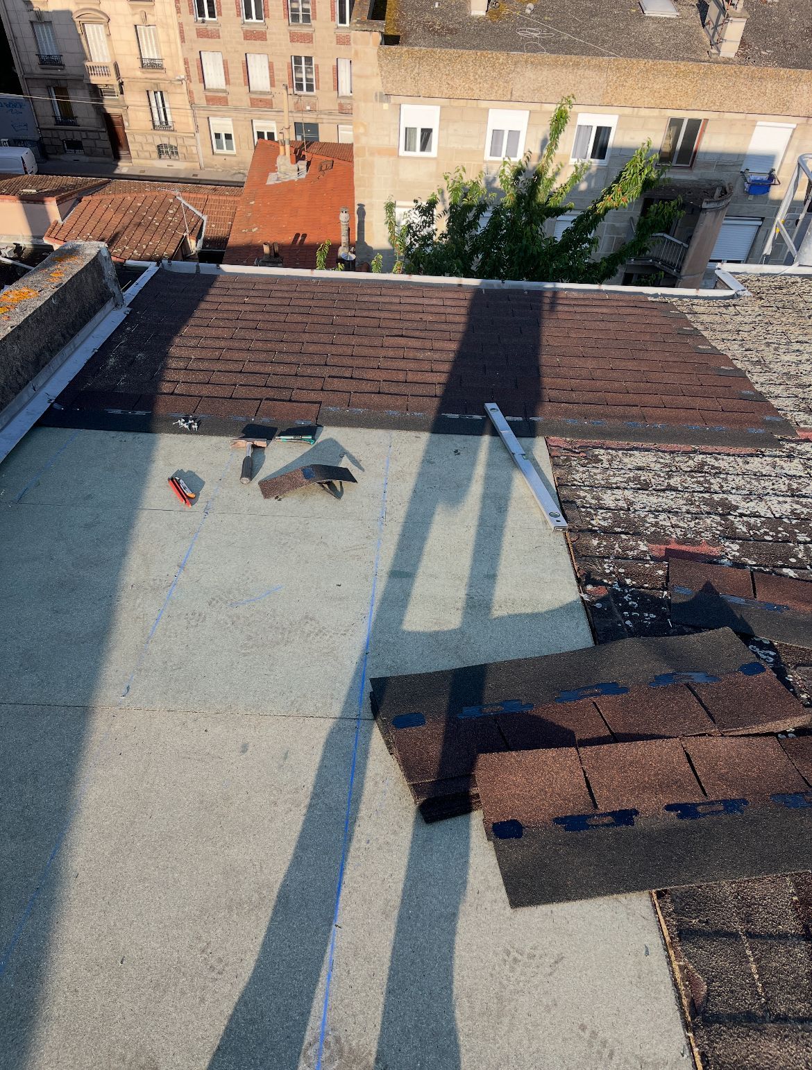 Vue depuis le toit avec gravier, parapets en briques, ombres et immeubles d'appartements à proximité.