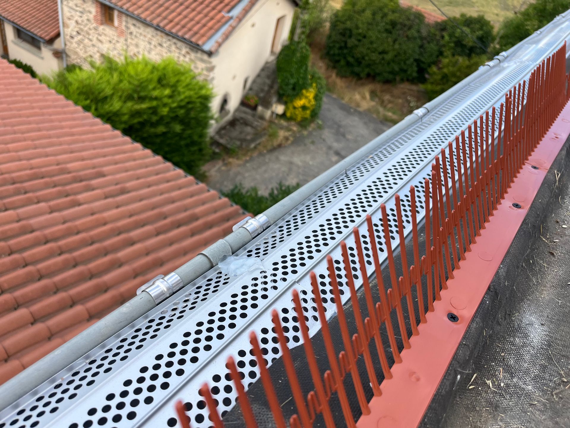 Bord de toit avec un garde-corps en métal perforé donnant sur des toits de tuiles rouges et une cour en contrebas.