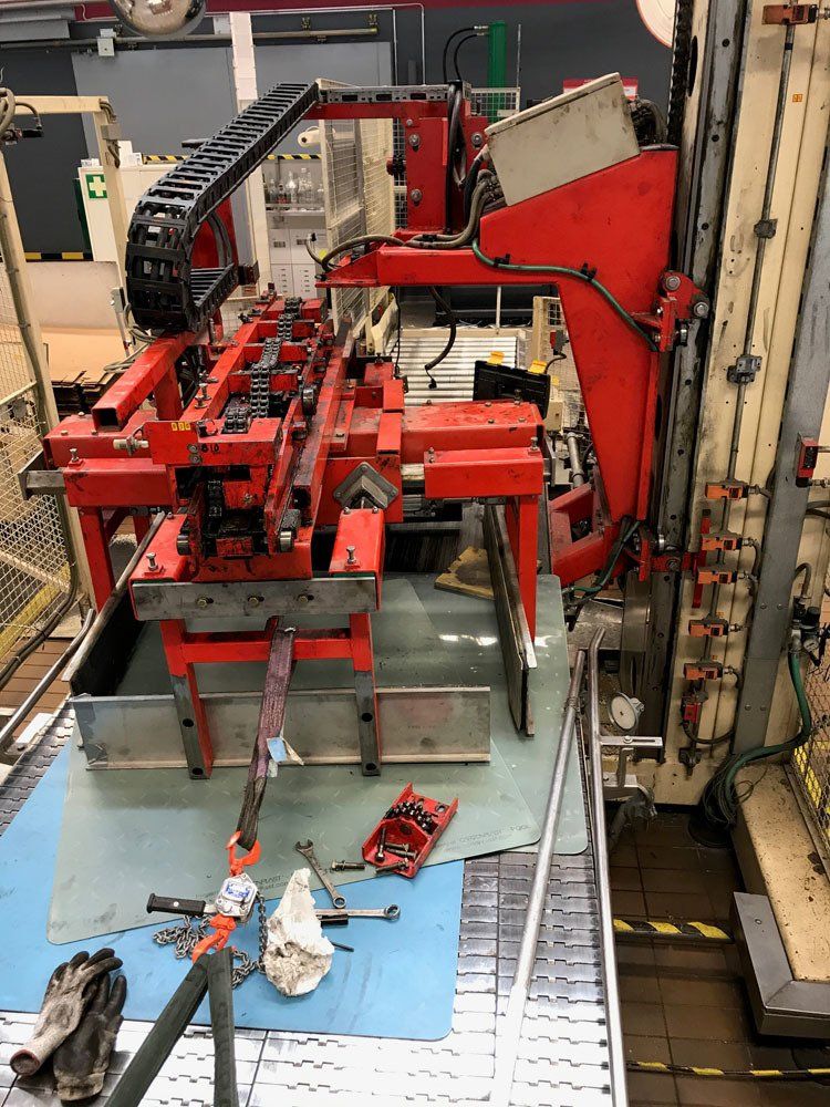 Punainen teollisuuskone seisoo tehtaan lattialla, ja lähellä on työkalutarjotin, puhdistusliina ja käsineet.