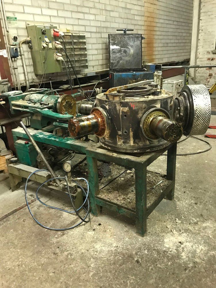 Suuri, teollinen metallikotelo on vihreällä metallityöpöydällä sekaisessa työpajassa, taustalla sorvi.