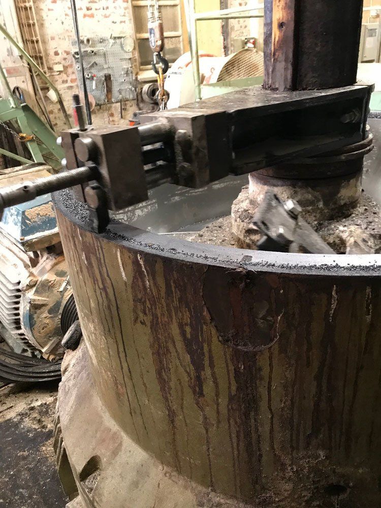 Lähikuva metallisesta teollisuussekoittimen varresta, joka on kiinnitetty suuren, lieriömäisen, tummalla jäännöksellä peittyneen astian reunaan.