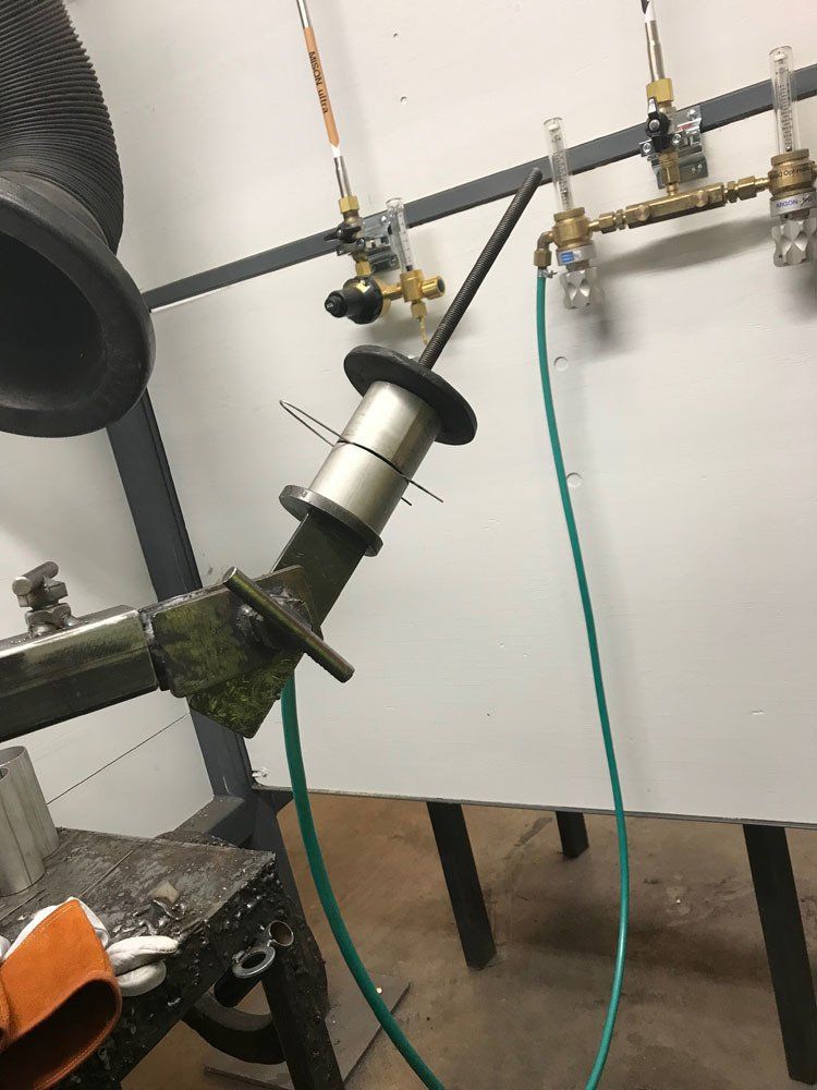 Mekaaninen varsi, jossa on sylinterimäinen metallikomponentti ja kiinnitetty vihreä letku työpajaympäristössä.