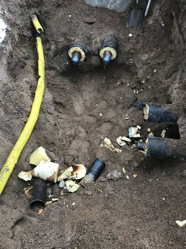 Avoin kaivanto maaperässä, joka sisältää useita eristettyjä mustia putkia ja pitkän, keltaisen muovikaapelin.