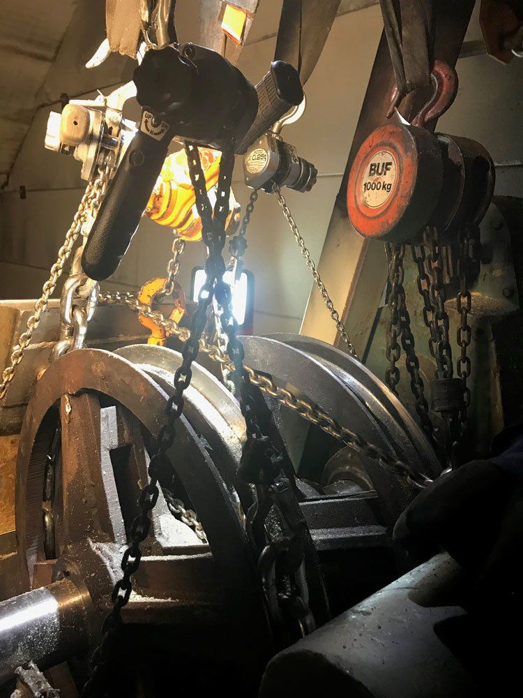 Suuri ketjujen varassa roikkuva teollinen hihnapyöräjärjestelmä hämärässä, metallisessa työpajassa.