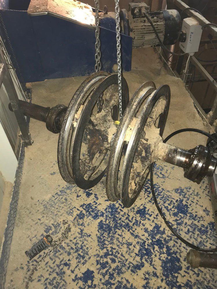 Kaksipyöräinen akselikokoonpano, joka on ripustettu ketjuilla kuvioidun lattian päälle työpajaympäristössä.