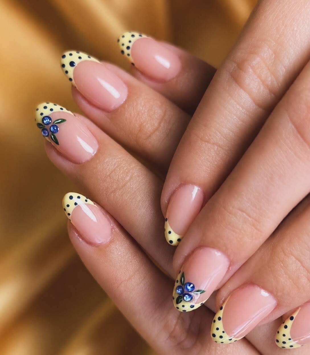 Manos con uñas rosas y manicura francesa con lunares amarillos y pequeños detalles florales azules.