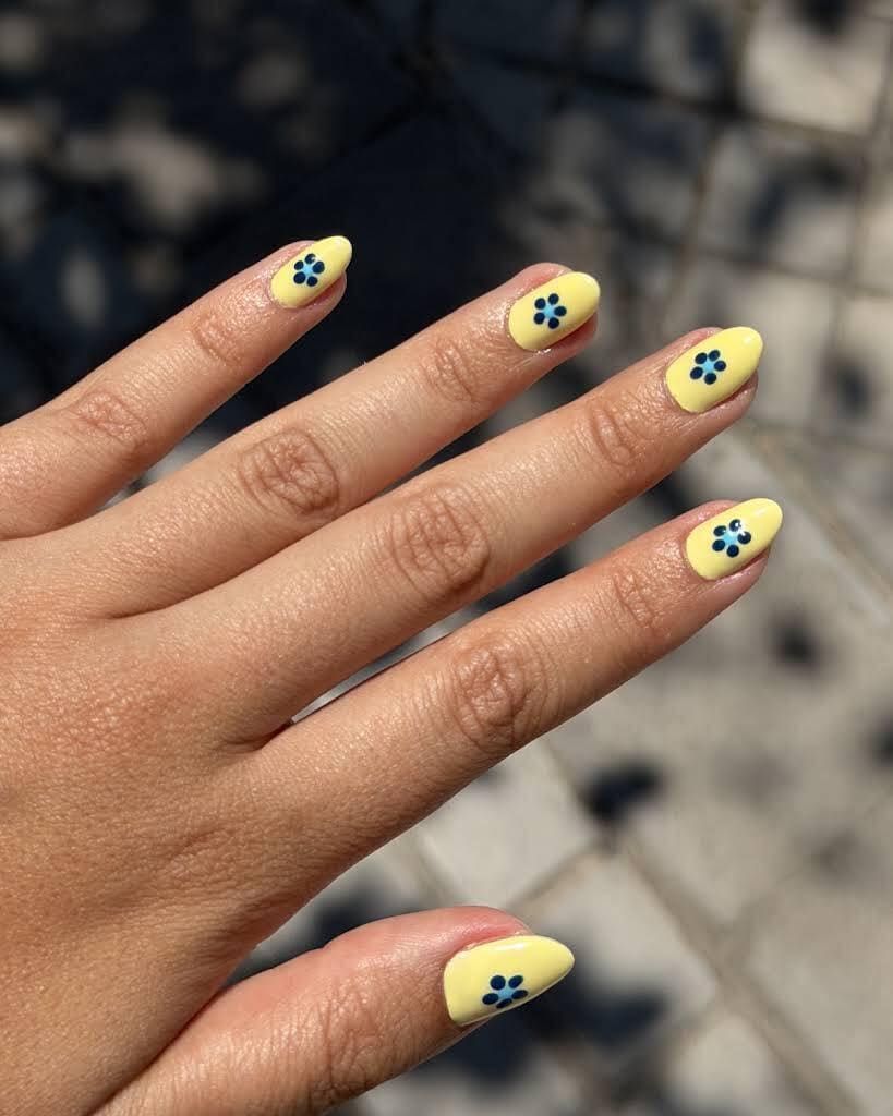 Mano con uñas amarillas y diseños de flores azules sobre un fondo borroso.